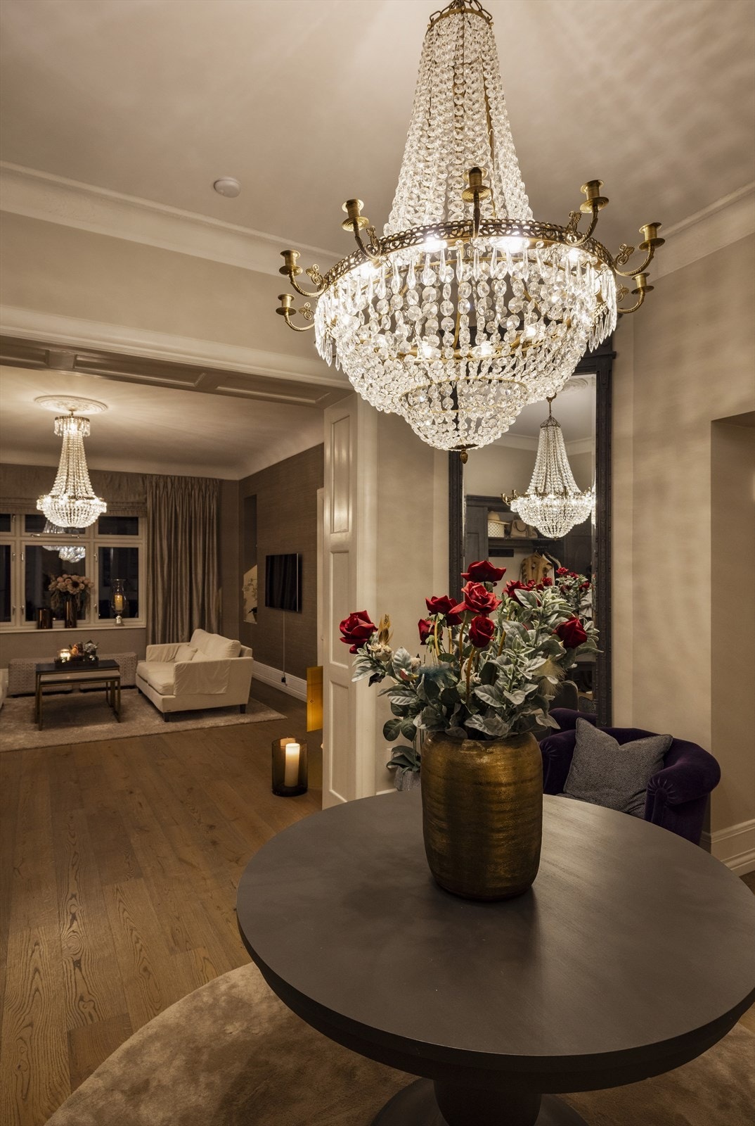 Den majestetiske lysekronen fyller rommet med varm glød og fremhever de brede døråpningene og detaljene rundt - diskret luksus i sitt rette element. Galleribilde