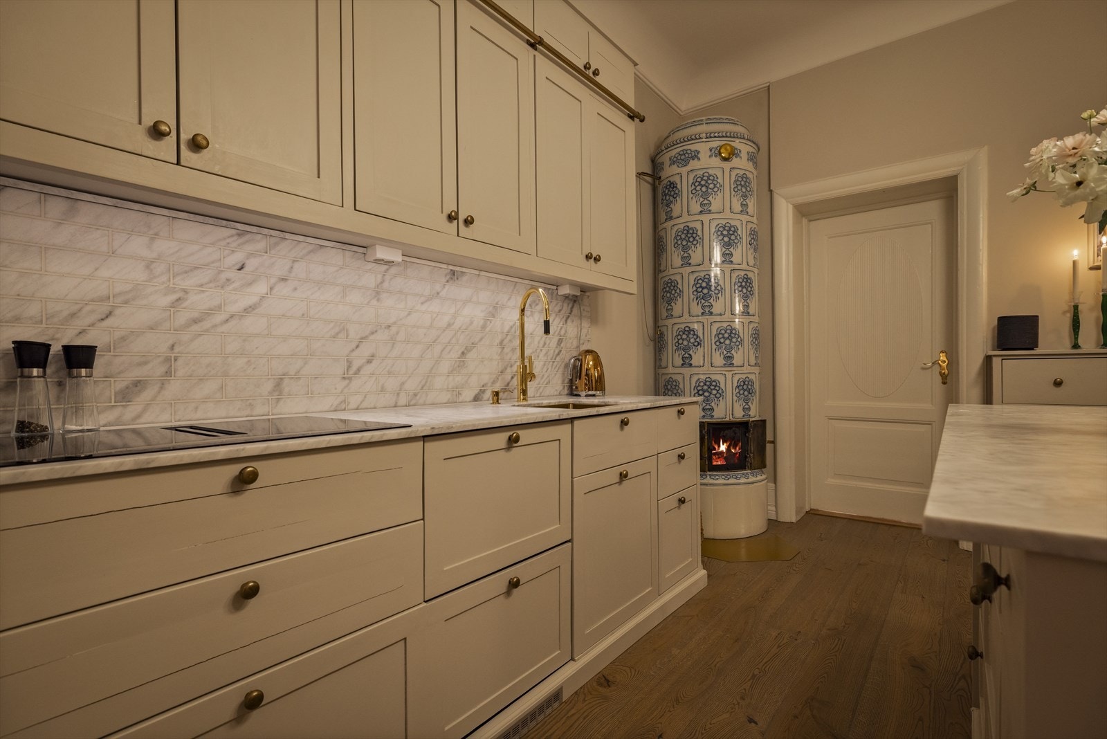 Kakkelovnens tidløse tilstedeværelse løfter rommet og binder sammen kjøkkenets klassiske og moderne elementer. Galleribilde