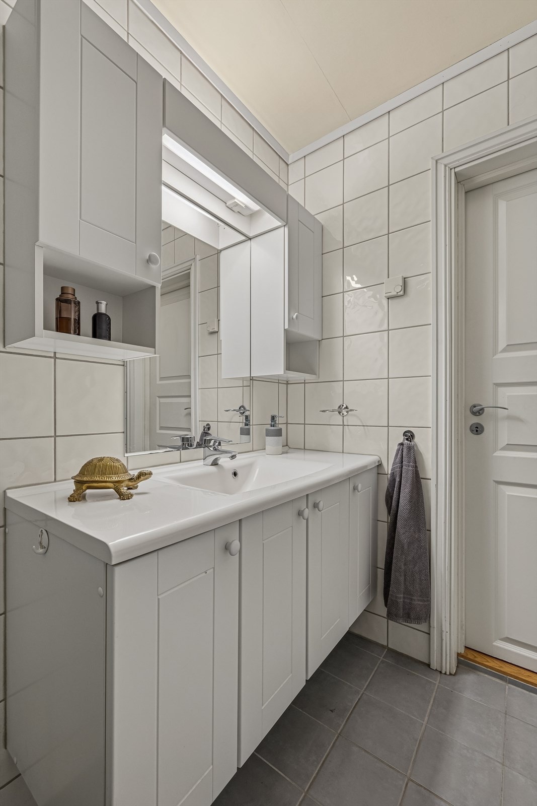 Badet er utstyrt med vegghengt toalett, dusjkabinett, servant med underskap, speil og et praktisk overskap som gir ekstra oppbevaringsplass. Galleribilde