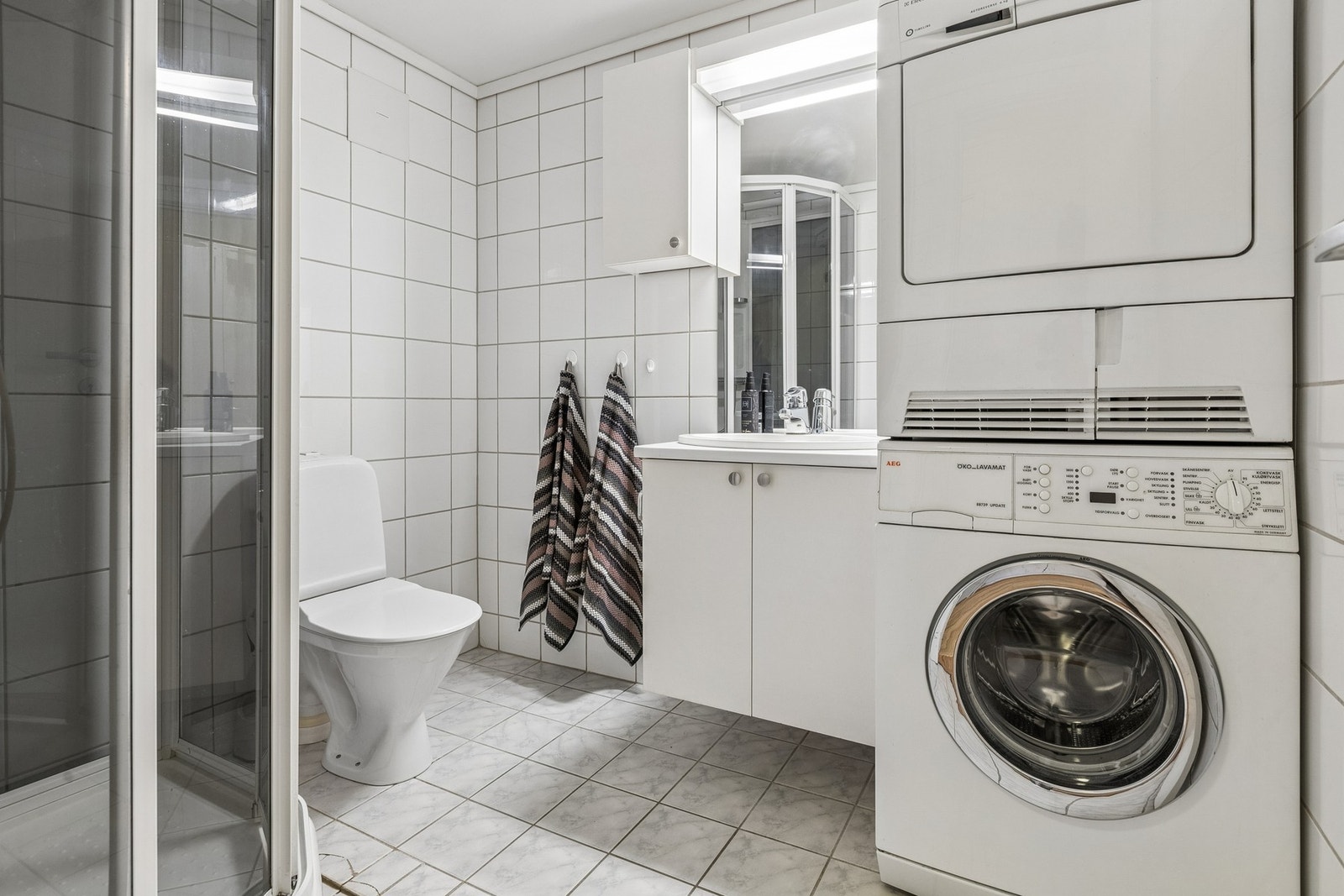 Badet er flislagt og utstyrt med dusjkabinett, toalett, servantinnredning med ovenpåliggende servant, speilskap og opplegg for vaskemaskin. Galleribilde