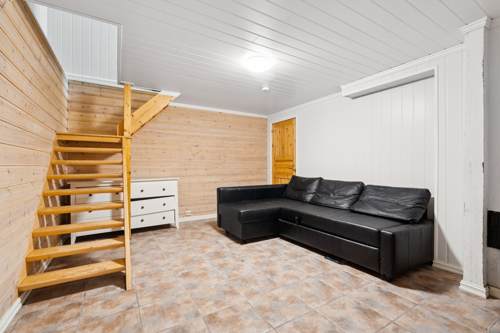 Kjellerstue med flislagt gulv og lakkert tretrapp som leder opp til første etasje. Galleribilde