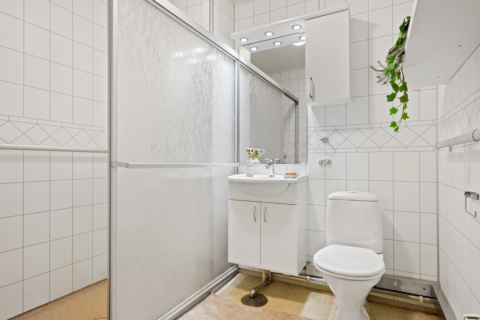 Bad med baderomsplater på vegg, vinylbelegg på gulv og dusjhjørne. Rommet har mekanisk avtrekk. Galleribilde