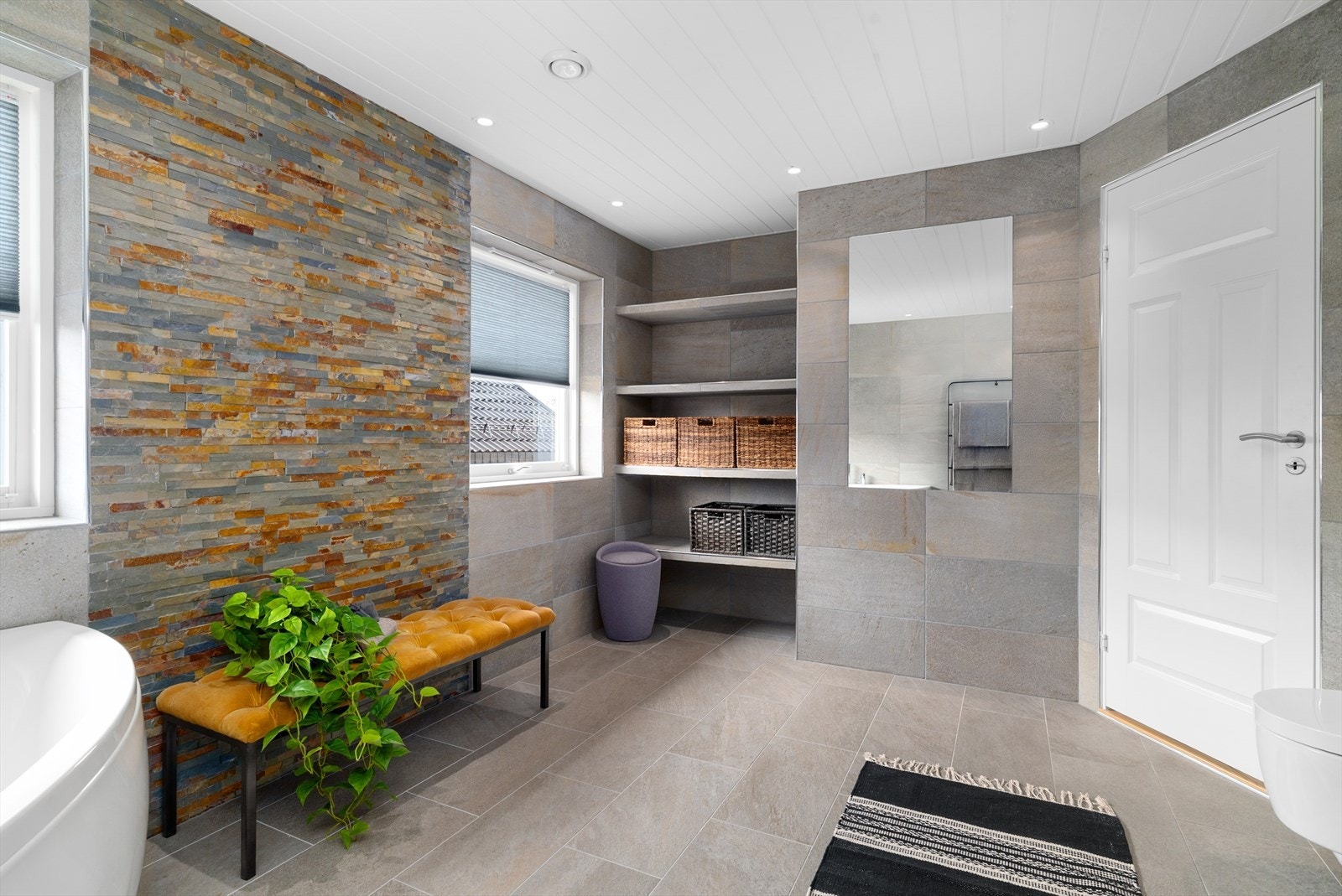 Badet er innredet med toalett, hjørnebadekar, dusjkabinett og servantinnredning med skuffer og speil. Det er også plassbygde hyller på vegg. Galleribilde