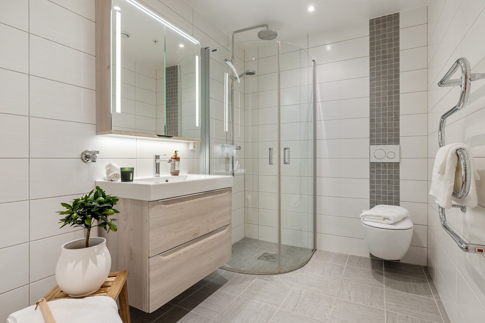 Badet er innredet med vegghengt toalett, servant med innredning, dusjhjørne og opplegg for vaskemaskin. Galleribilde