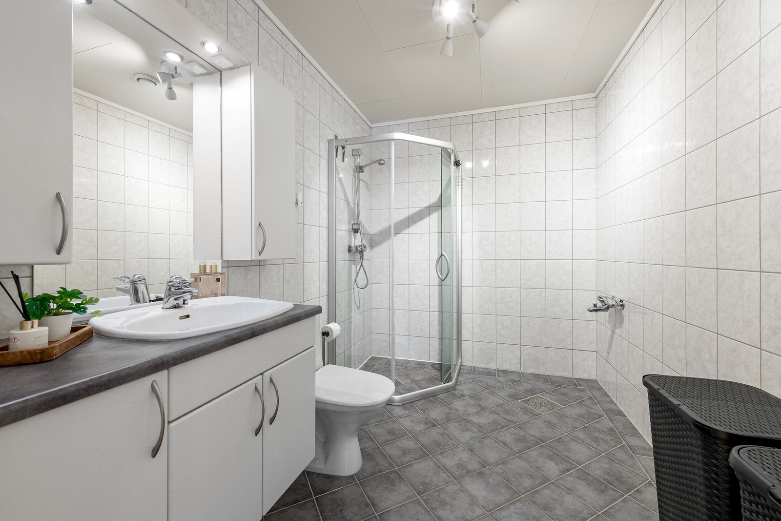 Badet har flislagt gulv med gulvvarme, flislagte vegger og et dusjhjørne med skyvedører. Rommet er klargjort for badekar. Galleribilde