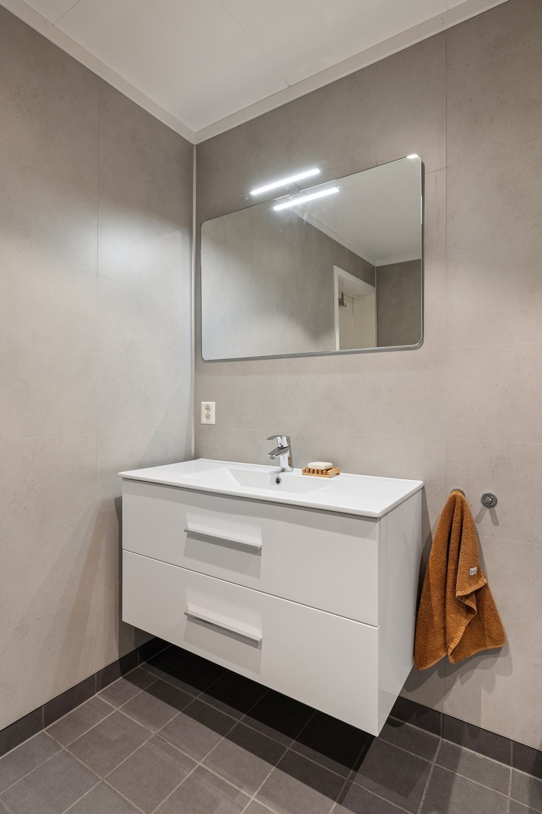 Badet har innredning med nedfelt servant, veggmontert toalett, dusjvegger/hjørne og opplegg for vaskemaskin. Galleribilde