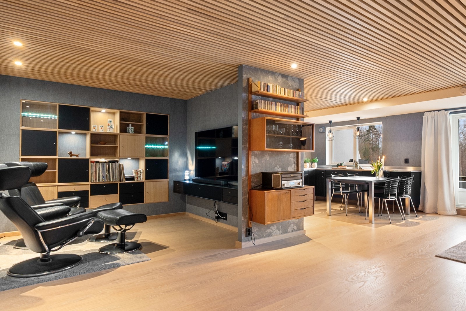 Stuen har flere soner for både sofagruppe, spisestue og en tilbaketrukket TV-stuedel med spesialtilpasset innredning. Galleribilde