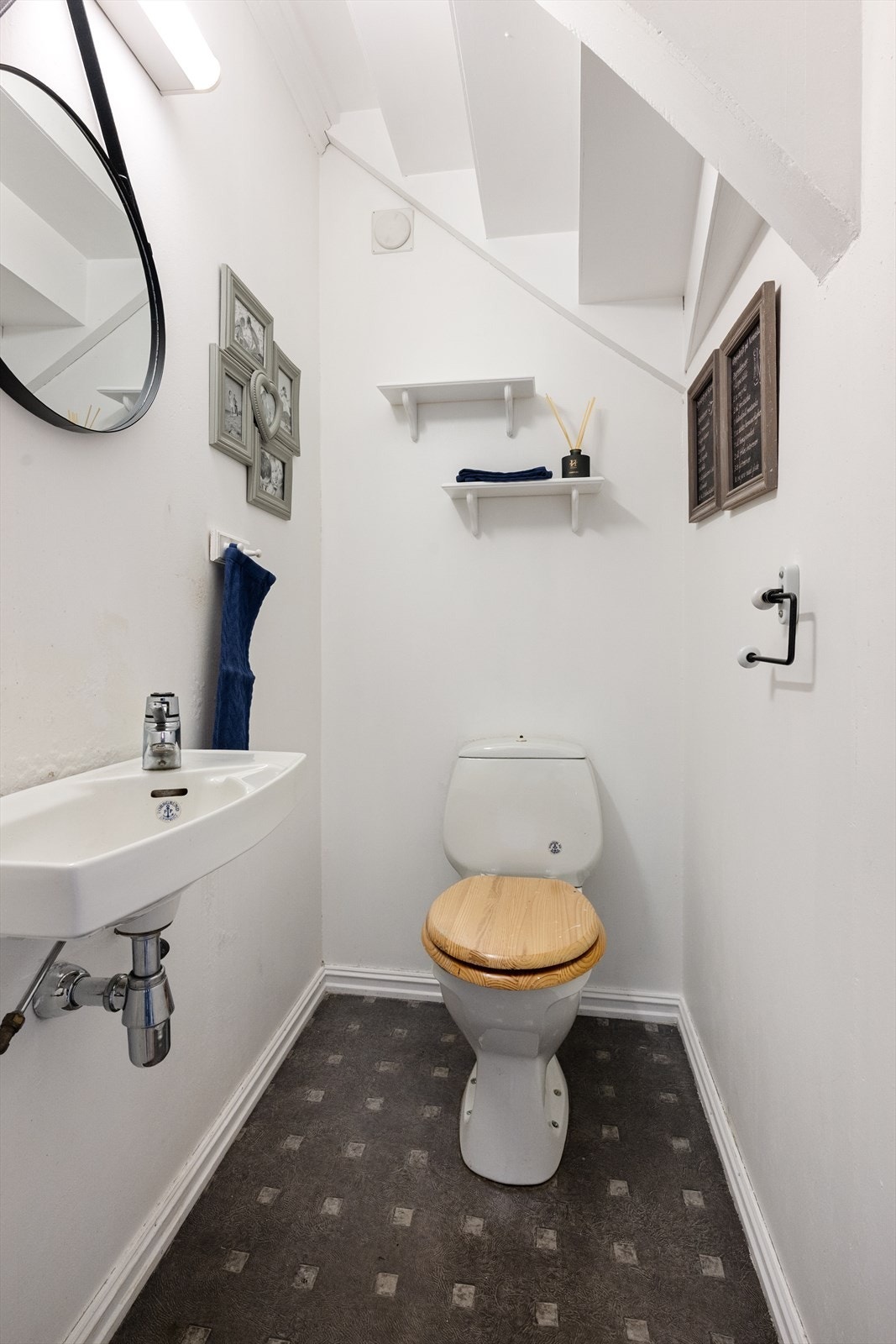 Boligen har eget toalettrom i 1. etasje, i tillegg til toalett på badet oppe. Toalettrommet har belegg på gulvet og for øvrig malte plater. Enkel servant og lys på vegg. Galleribilde