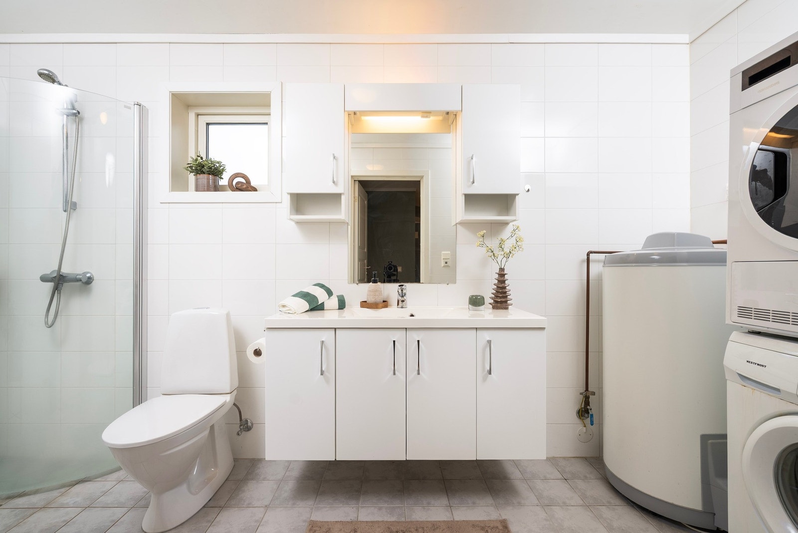 Flislagt bad med varmekabler i gulvet, god oppbevaringsplass i servantinnredning, og opplegg til vaskemaskin og tørketrommel Galleribilde