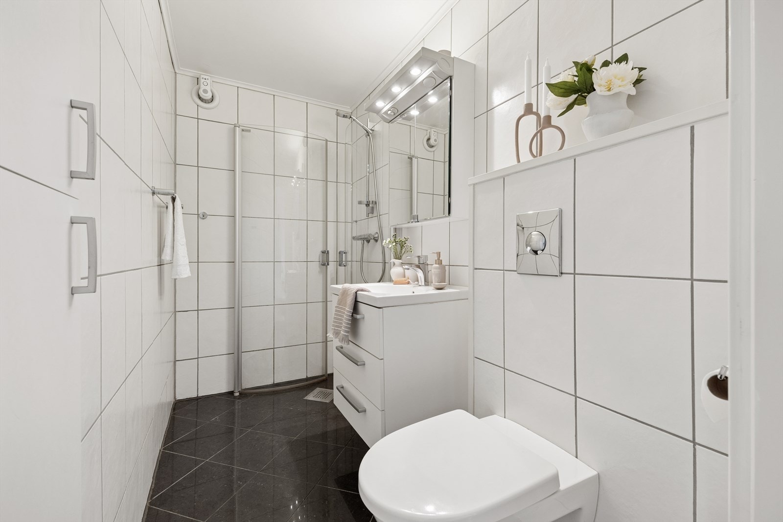 Delikat flislagt bad utstyrt med dusjhjørne, vegghengt toalett og moderne baderomsinnredning. Galleribilde