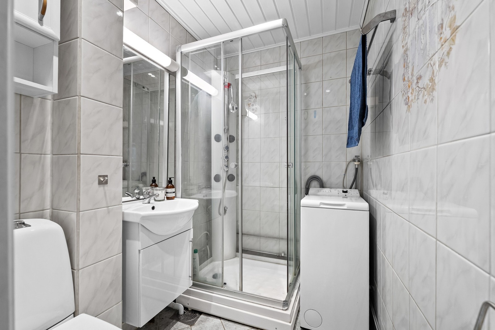 Flislagt bad med varmekabler i gulv og servantskap med speil over, samt skap over gulvstående toalett. Videre er badet utstyrt med dusjkabinett og opplegg for vaskemaskin. Galleribilde