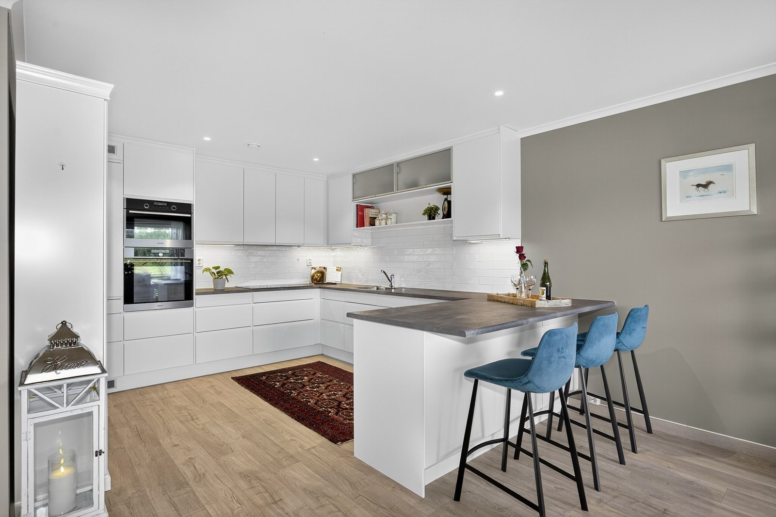 Kjøkkendelen har en stilren innredning med takhøye skap og slette fronter. Det er laminat benkeplate og flis over kjøkkenbenk. Mot stuedelen er det tillaget en hyggelig frokostplass. Galleribilde