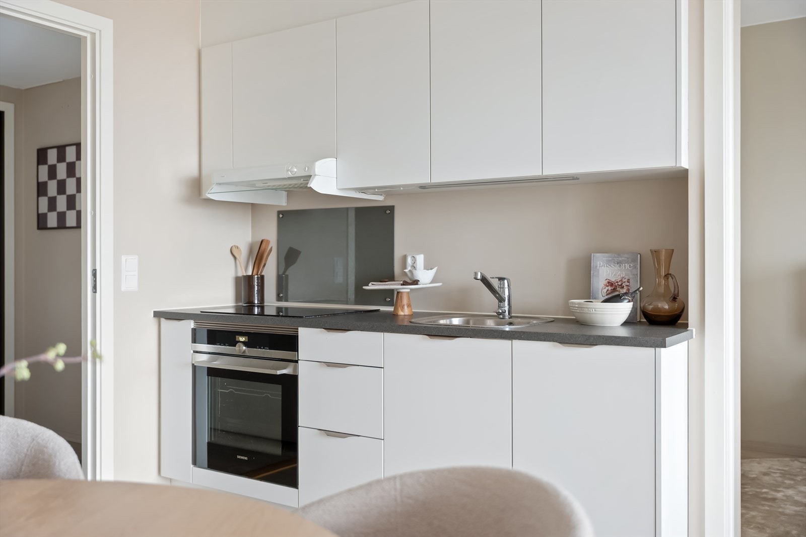 Stilrent og funksjonelt kjøkken med integrerte hvitevarer som platetopp, stekeovn, oppvaskmaskin og kjøl/frys. Galleribilde