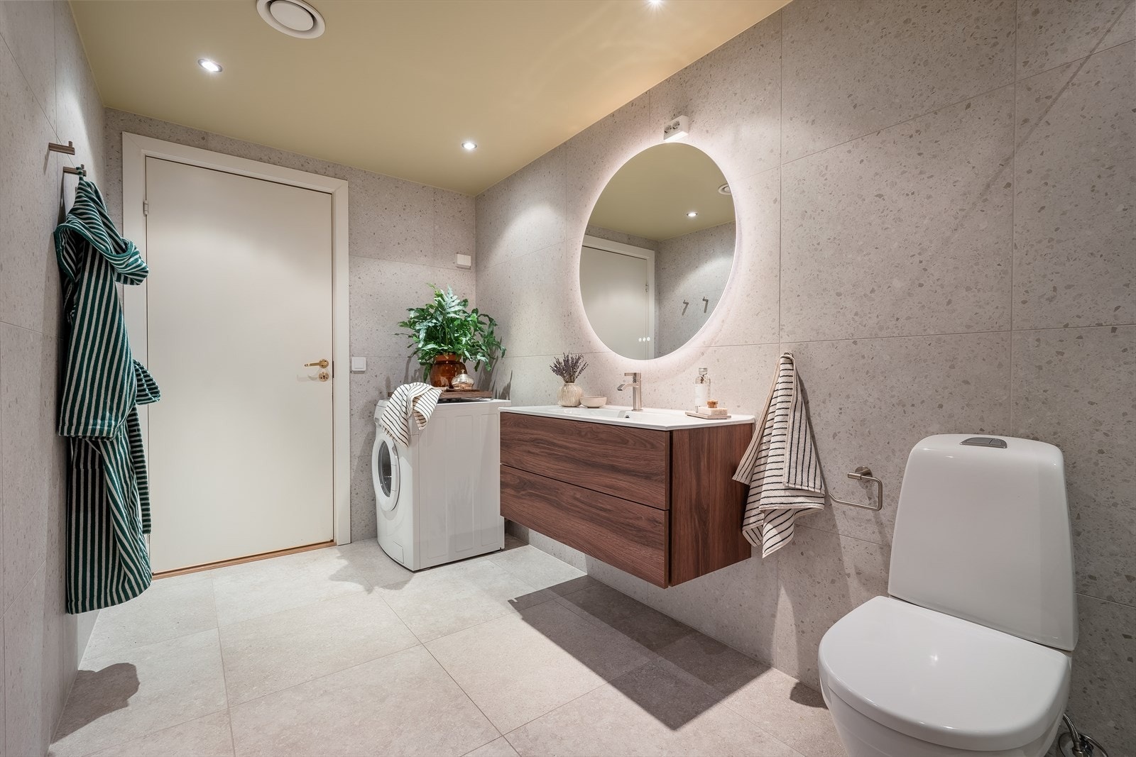 Badet er innredet med servant på servantskap, toalett, speil med innebygget lys og dusjhjørne. Alt av baderomsgarnityr er fra kvalitetsmerket tapwell. Det er opplegg for vaskemaskin og tørketrommel i hjørnet. Galleribilde