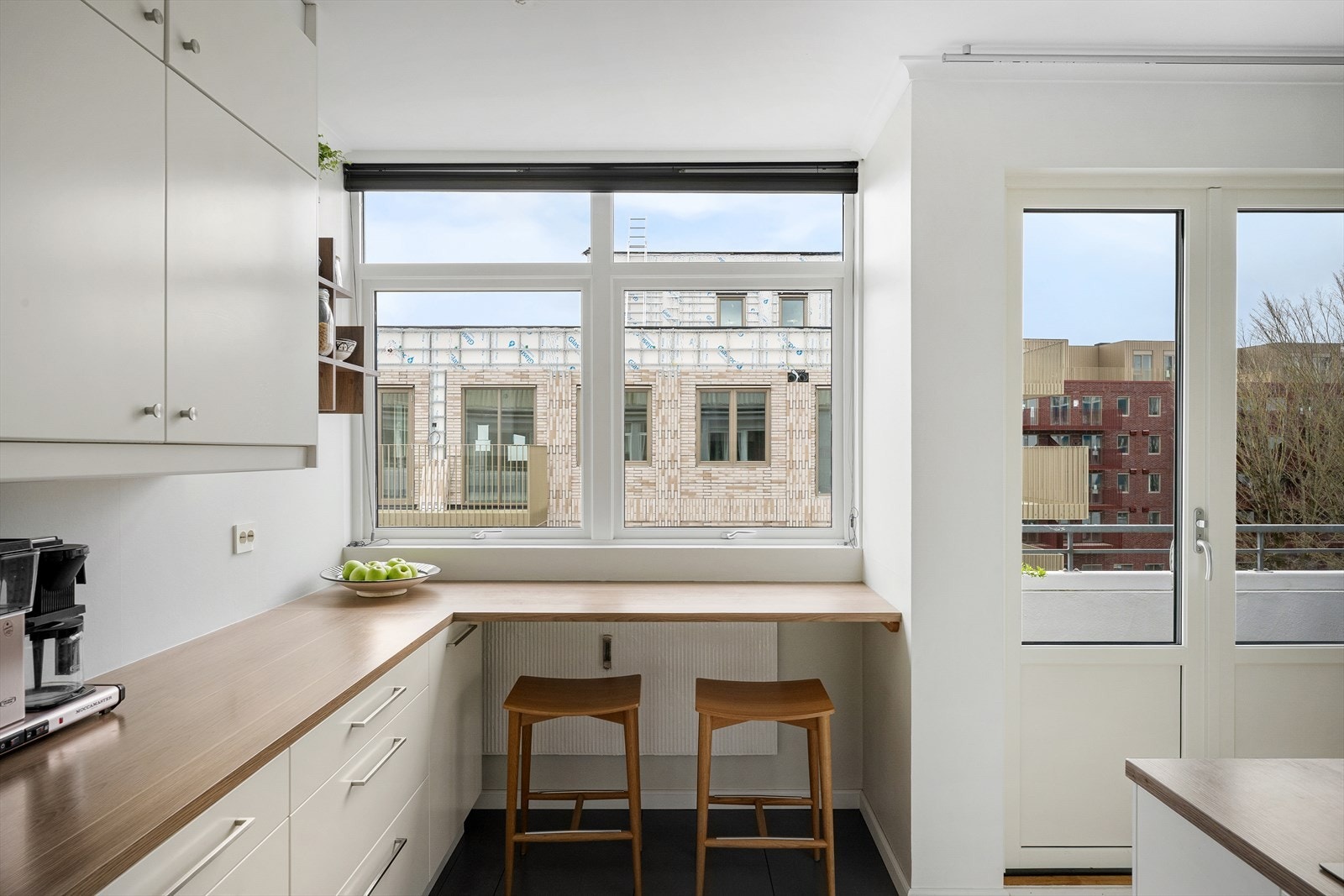 Kjøkkenet er trukket tilbake og delvis adskilt, men i åpen løsning. Et kjøkken du får lyst å være på, både kokken og den som skal skravle. Her har du to barstoler med bord/benk i vinduskarmen - så dere kan nyte en kaffekopp og PC eller utsikt bynutene. Galleribilde