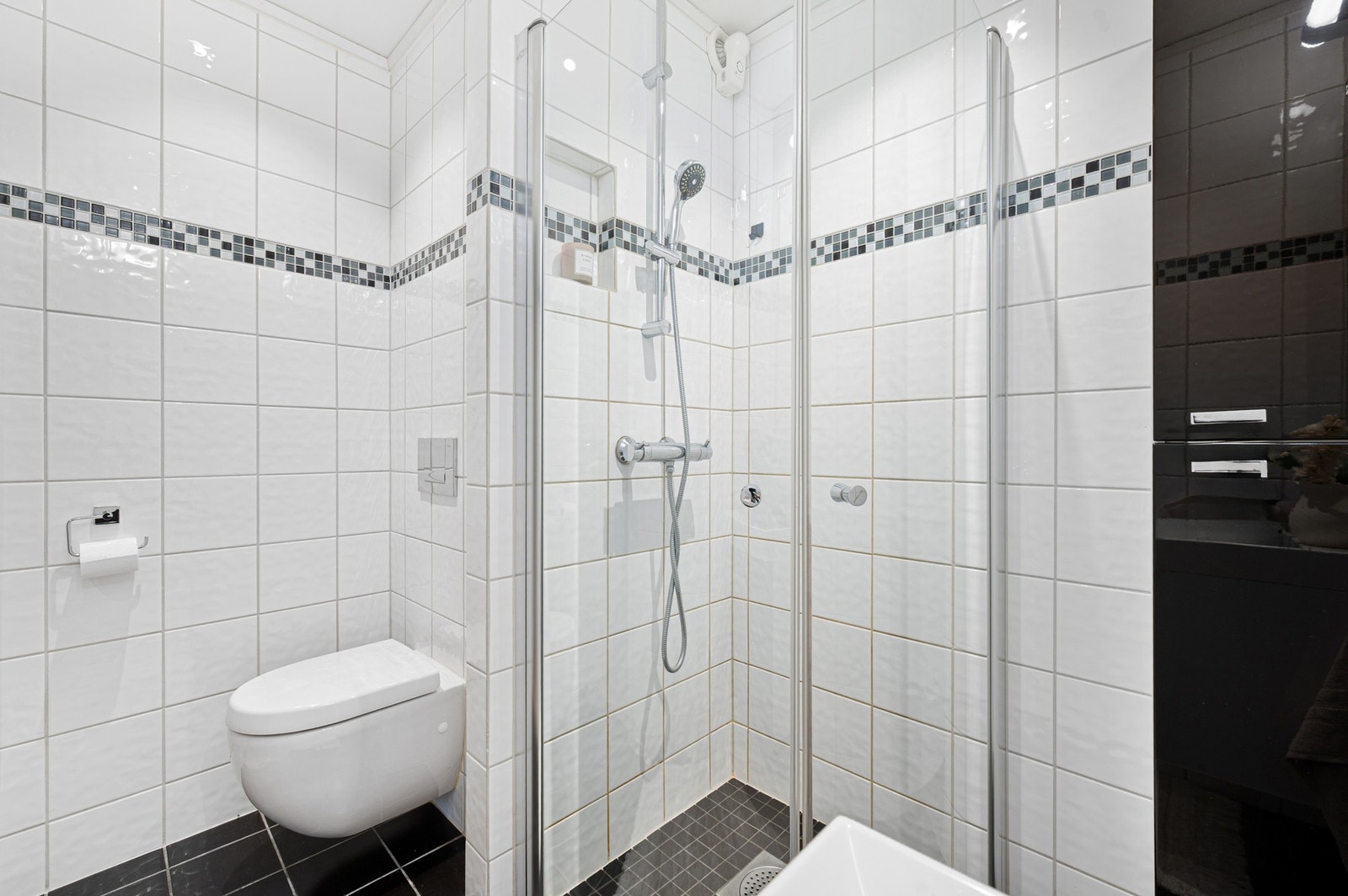 Rommet har en åpen dusjplass med innfellbare dusjdører, vegghengt WC og matchende baderomsinnredning. Galleribilde