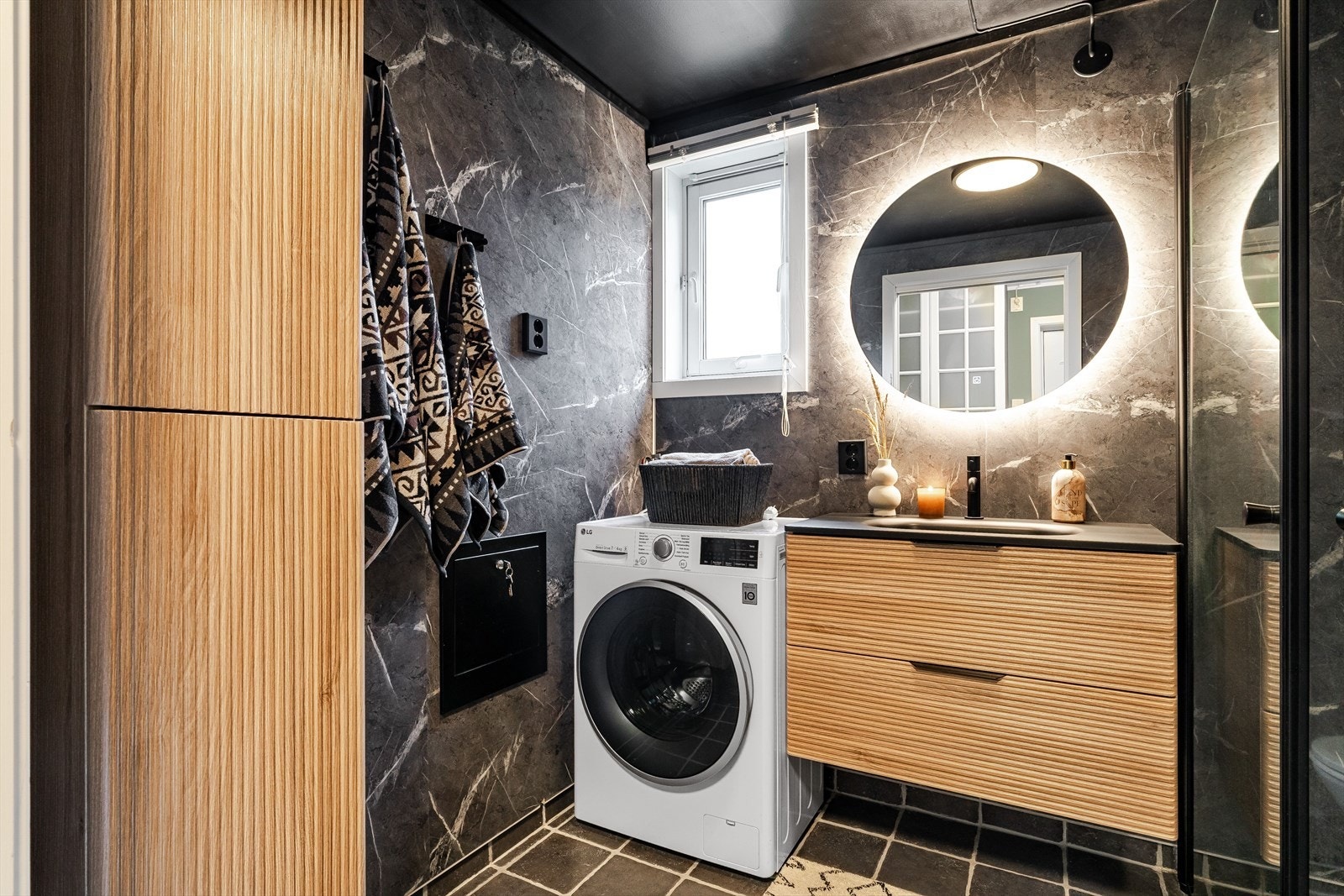 Badet har moderne innredning, mørke overflater, varmekabler i gulv og opplegg for vaskemaskin. Galleribilde