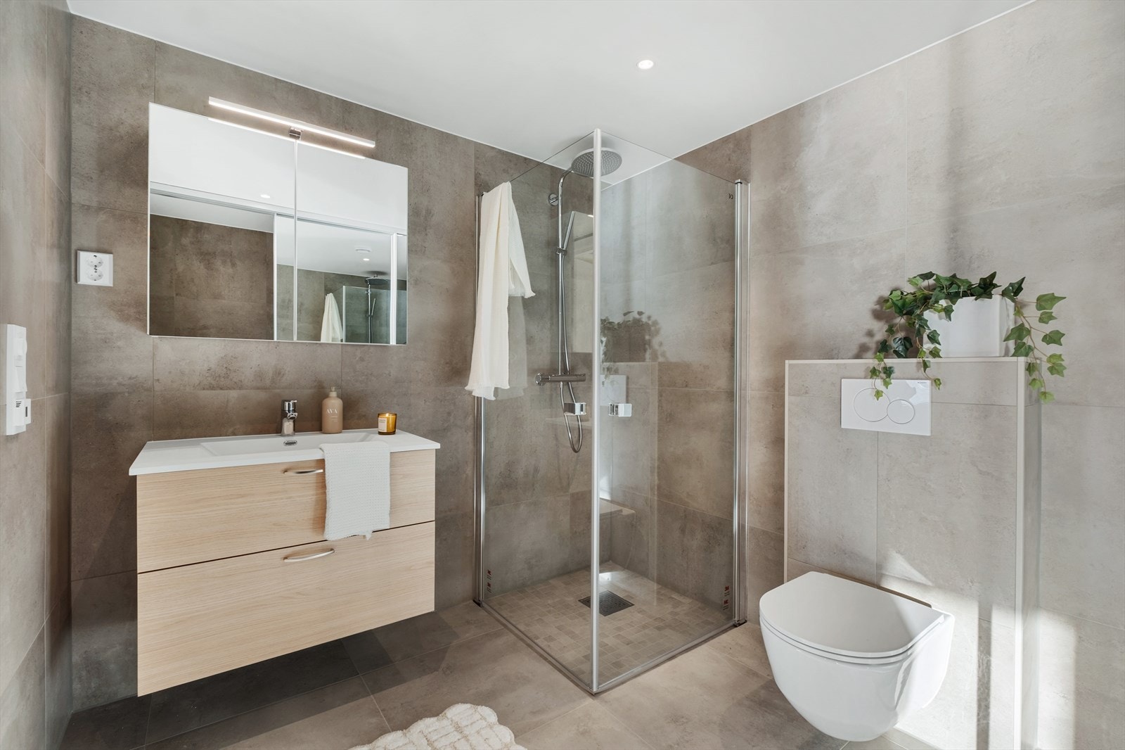 Badet er videre utstyrt med vegghengt toalett og dusjhjørne med glassvegger, noe som skaper en funksjonell og stilren løsning Galleribilde