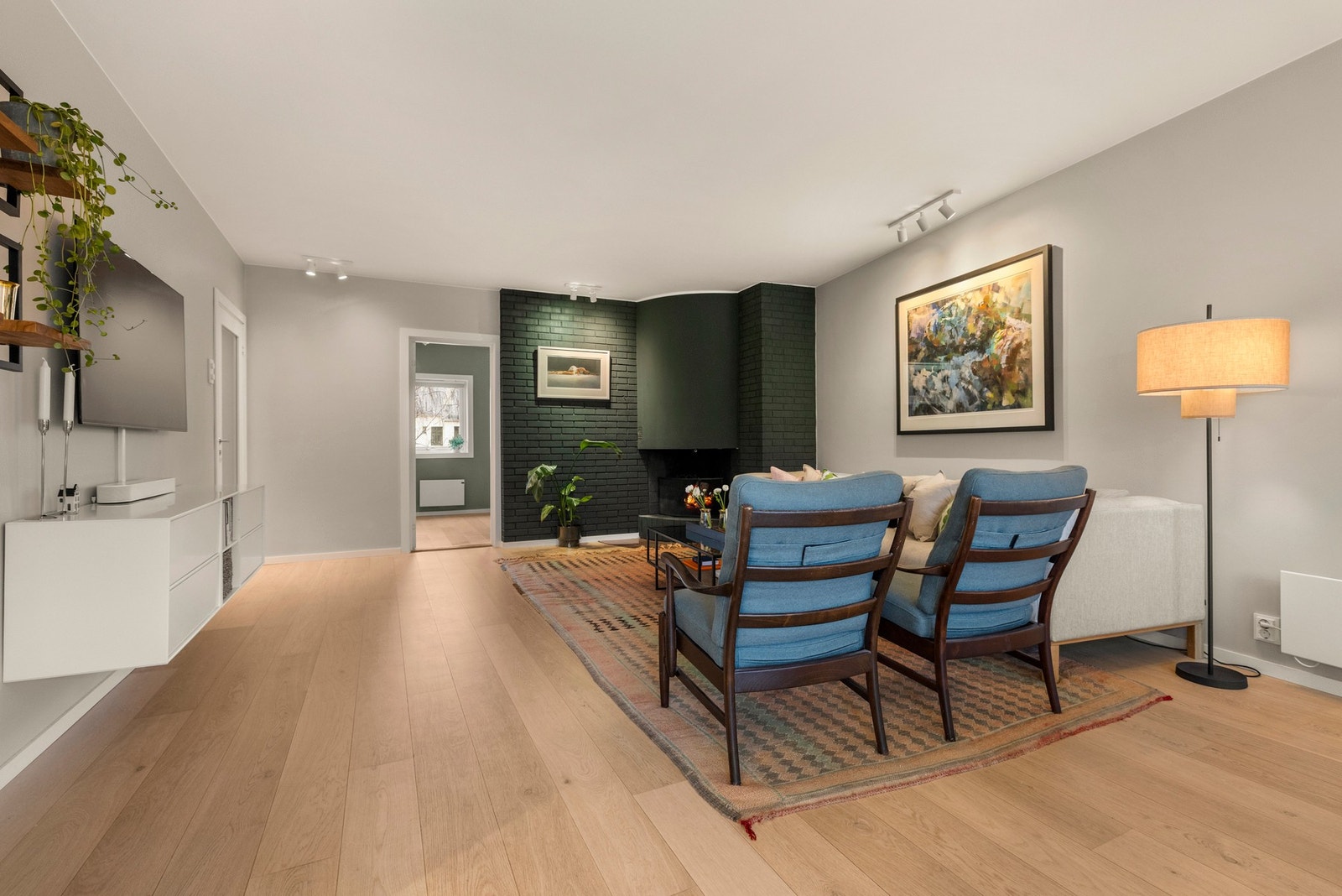 Stilig murt hjønepeis. Ildstedet og teglsteinen bak er malt i en dyp grønntone, i fin kontrast til gråmalte veggflater ellers. Galleribilde