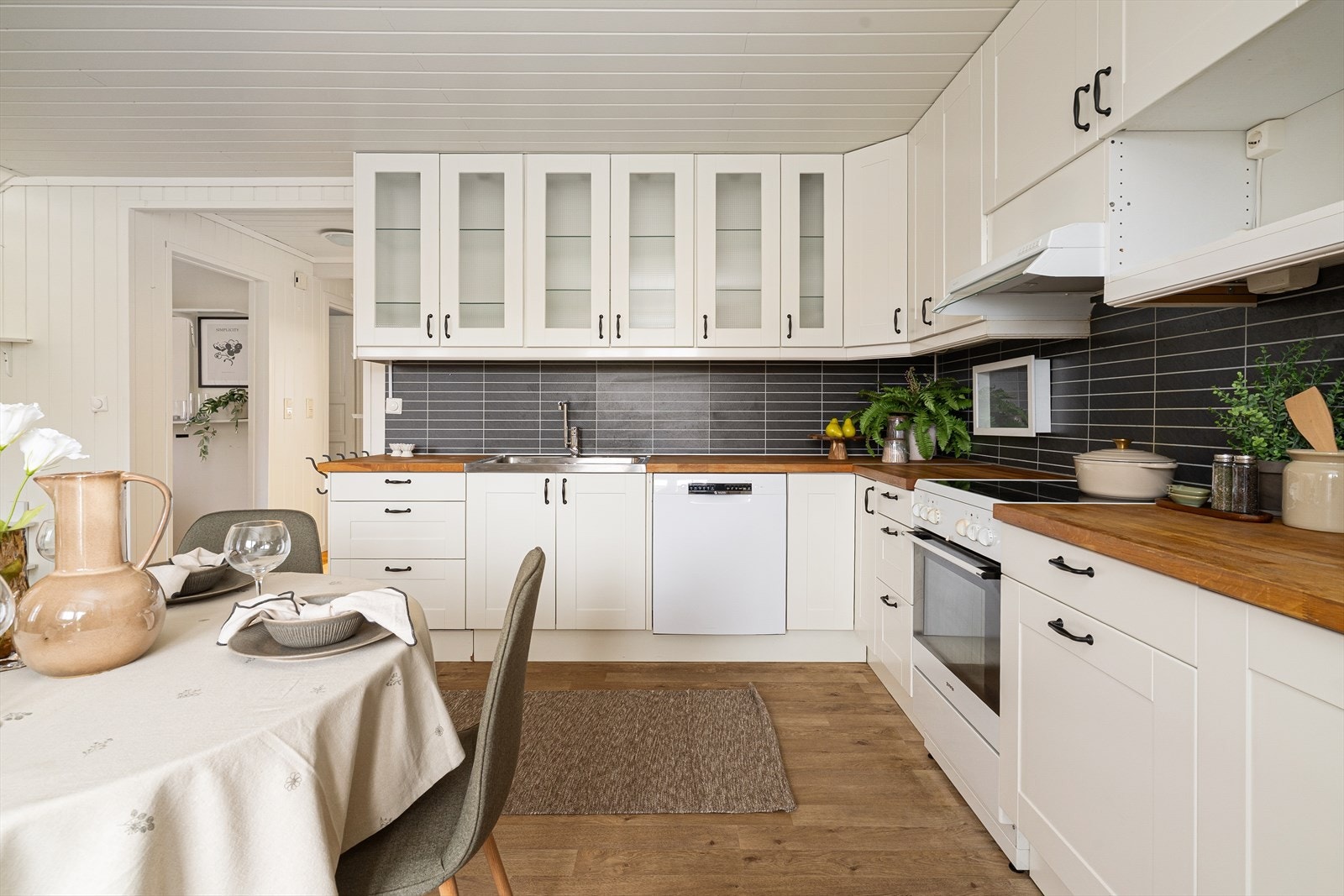 Kjøkkenet har godt med oppbevaringsplass i hvit innredning med takhøye overskap hvor det også er innslag av glass-skap. Det er også gode arbeidsflater på benkeplate i heltre. Galleribilde