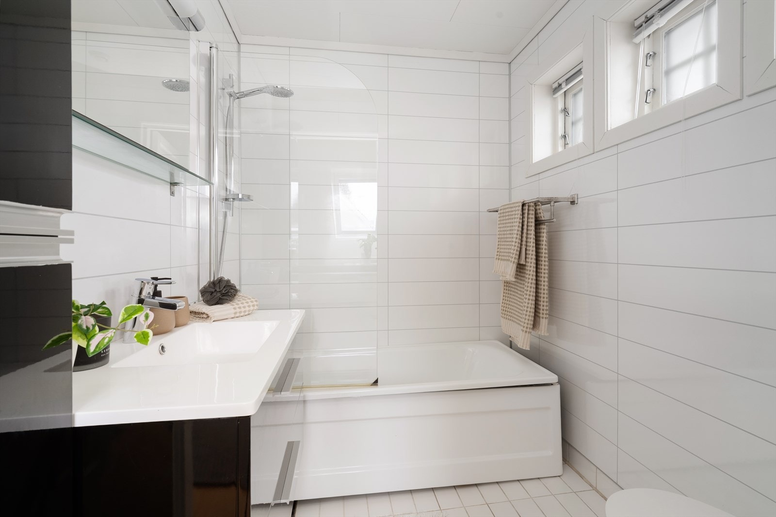 Mens badet nede har dusjnisje, er badet i 2. etasje innredet med badekar, med glassvegg og dusjgarnityr på vegg. Galleribilde