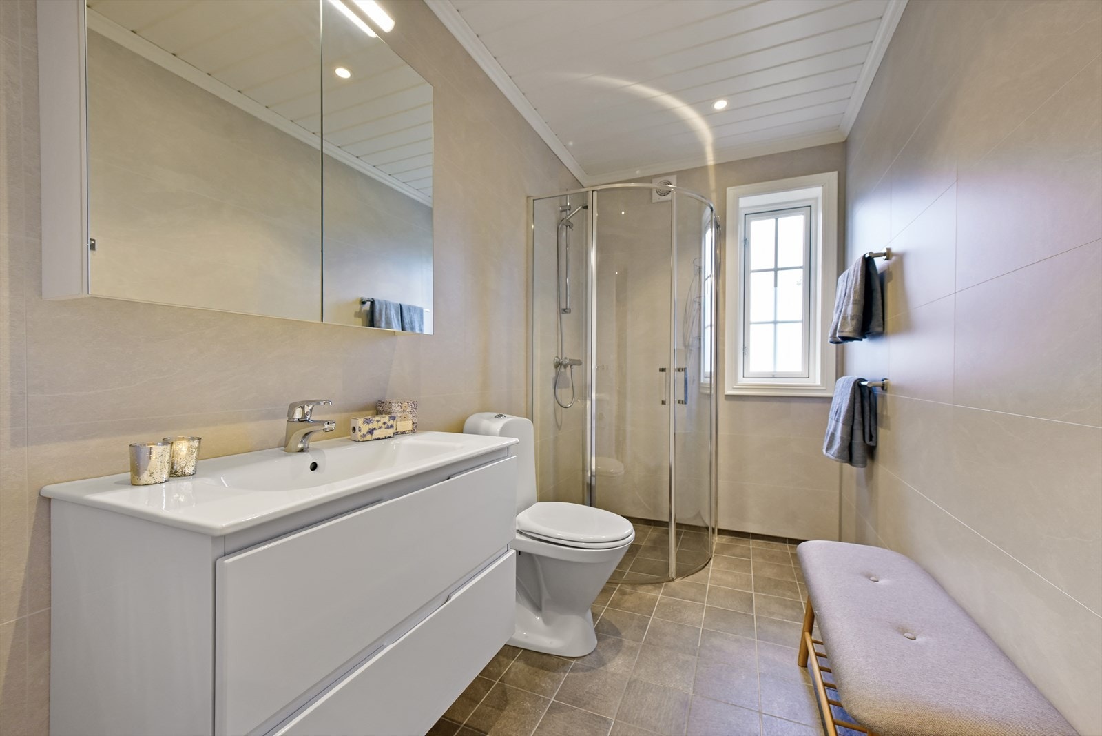 Badet har flislagt gulv med varmekabler, våtromsplater på veggene og downlights i taket. Galleribilde