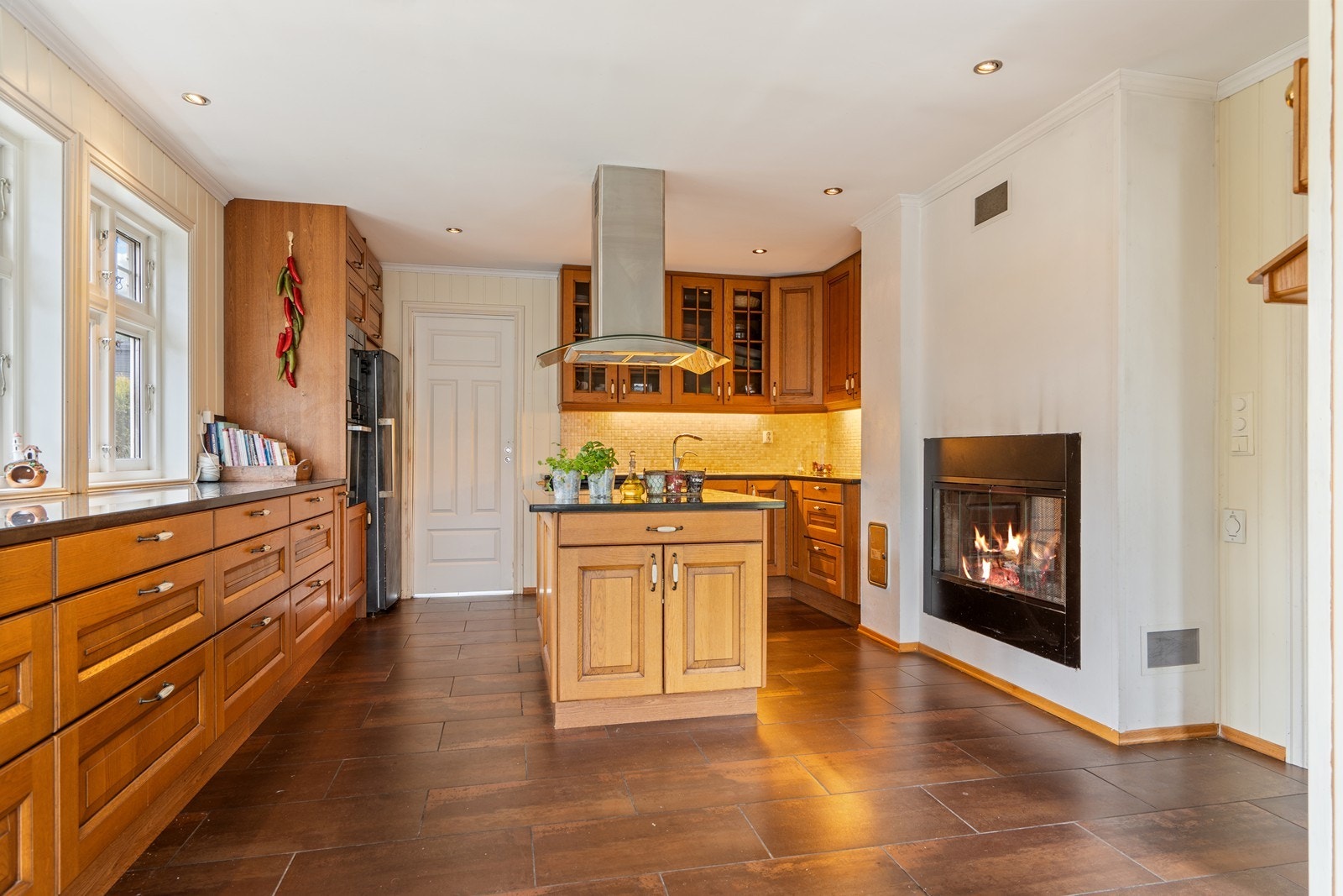 Flott kjøkkeninnredning med profilerte fronter og benkeplate i stein. Gjennomgående peis i vegg Galleribilde