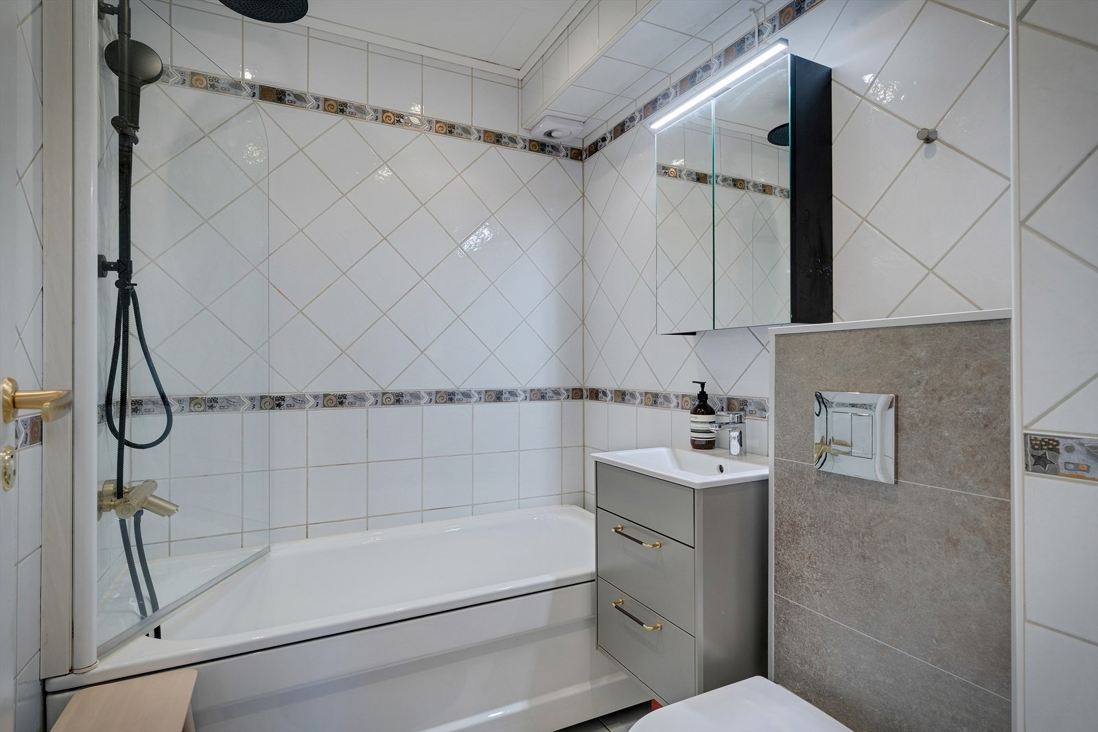 Flislagt bad utstyrt med badekar, vegghengt toalett og servantinnredning. Galleribilde