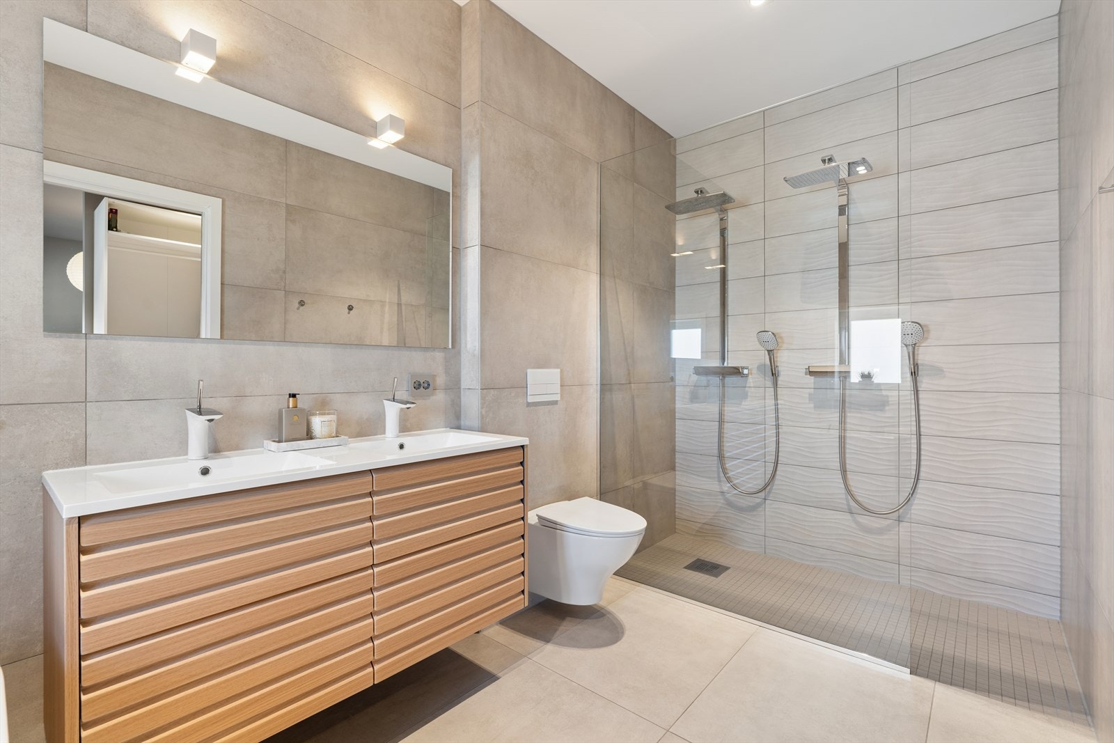 Badet er innredet med vegghengt toaltett, lekker dobbeltdusj med glassvegg, badekar, samt baderomsinnredning med dobbel servant og stort speil. Galleribilde