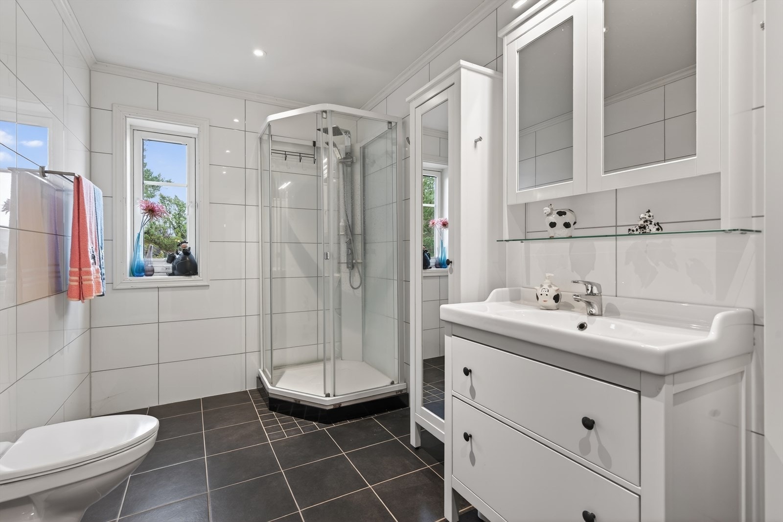 Badet i 1. etasje har fliser på gulv og vegg. Rommet er utstyrt med dusjkabinett, seksjon med servant og vegghengt toalett. Galleribilde