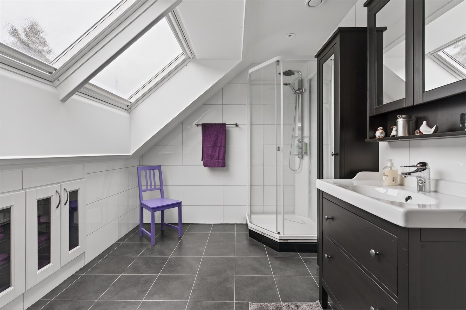 Badet i loftsetasjen har fliser på gulv og vegg. Rommet er utstyrt med dusjkabinett, seksjon med servant og vegghengt toalett. Galleribilde