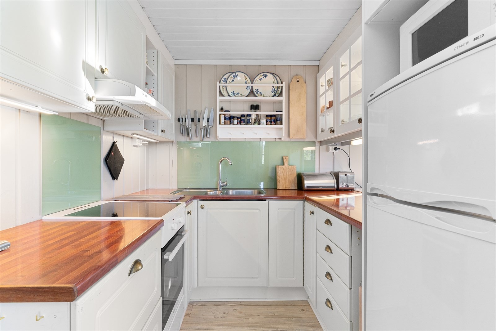 Kjøkkeninnredningen har hvite profilerte fronter, laminert benkeplate, vaskekum i stål, komfyr, ventilator. Det er kjøkkenventilator med avtrekk ut. Galleribilde