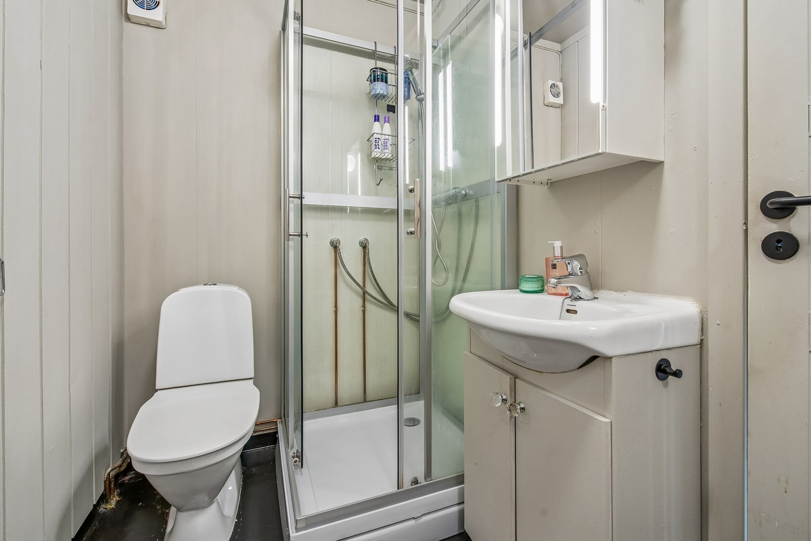 Badet er funksjonelt innredet med dusjkabinett, gulvmontert toalett og servant med underskap. Galleribilde