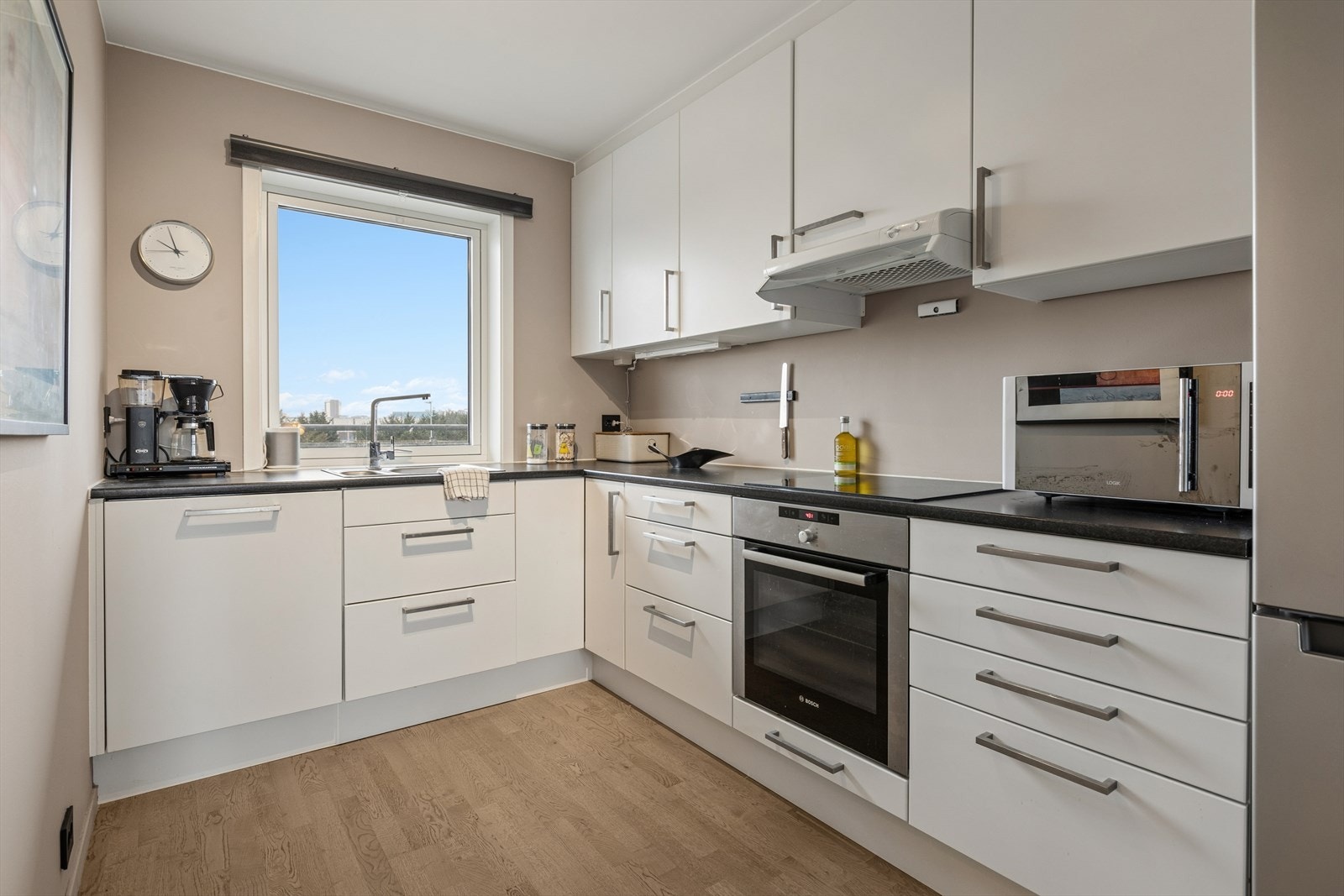 Kjøkkenet er stilrent innredet med hvite, slette fronter og grå benkeplate i laminat. Et godt utnyttet kjøkken hvor man har rikelig med lagringsplass i skap og skuffer. Galleribilde