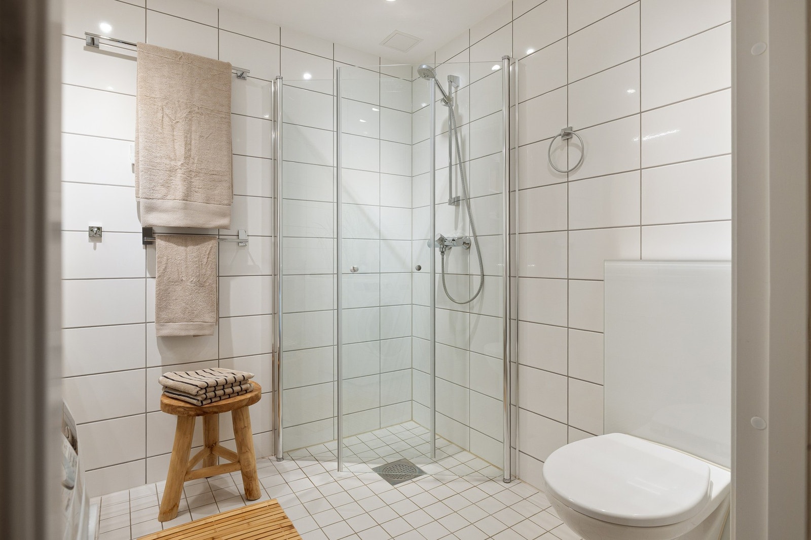 Baderommet er også utstyrt med dusjhjørne med innfellbare glassdører og veggmontert hånddusj, samt vegghengt toalett. Galleribilde