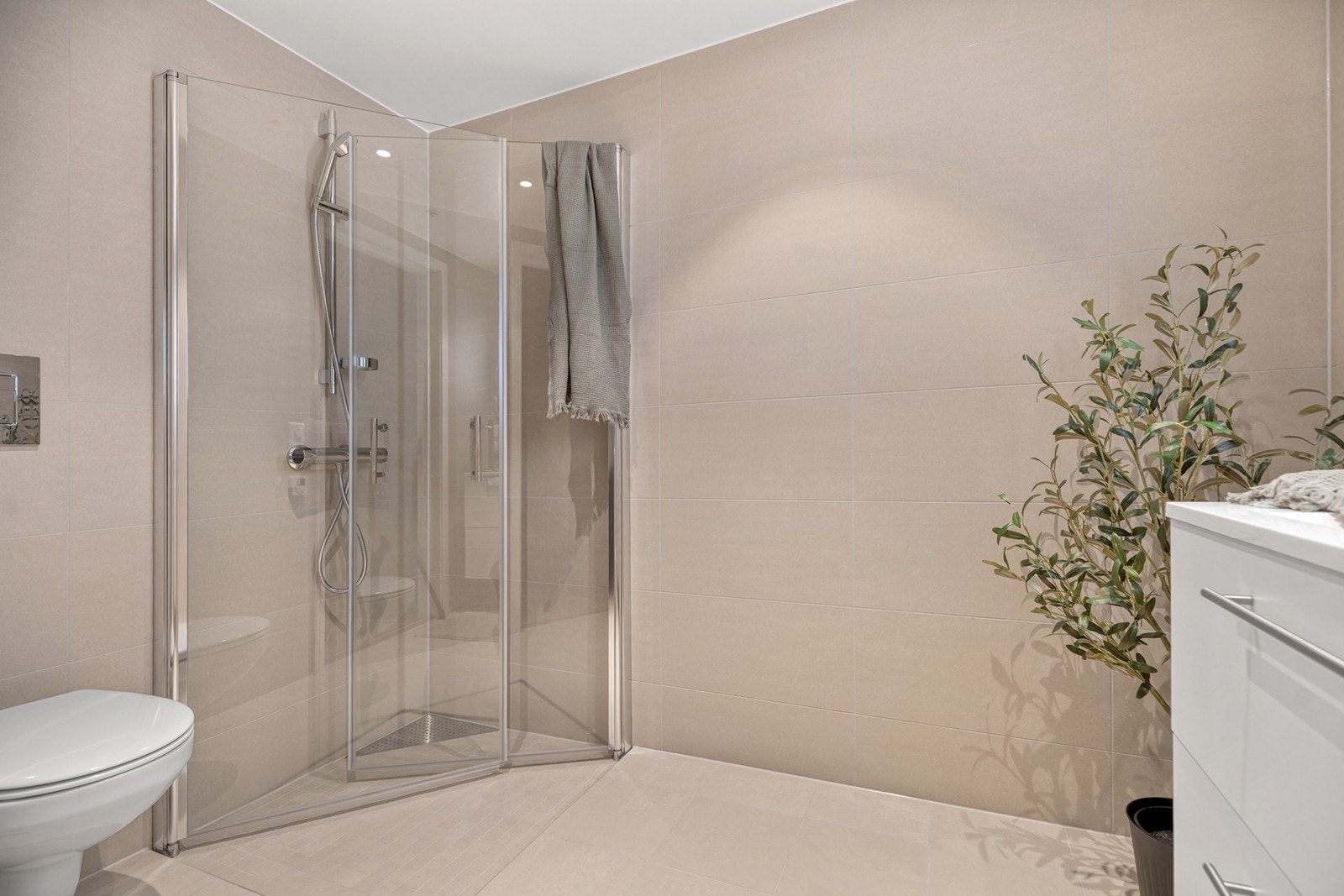 Badet er pent innredet med dusjhjørne, veggmontert toalett og heldekkende servant i baderomsinnredning. Opplegg for vaskemaskin Galleribilde