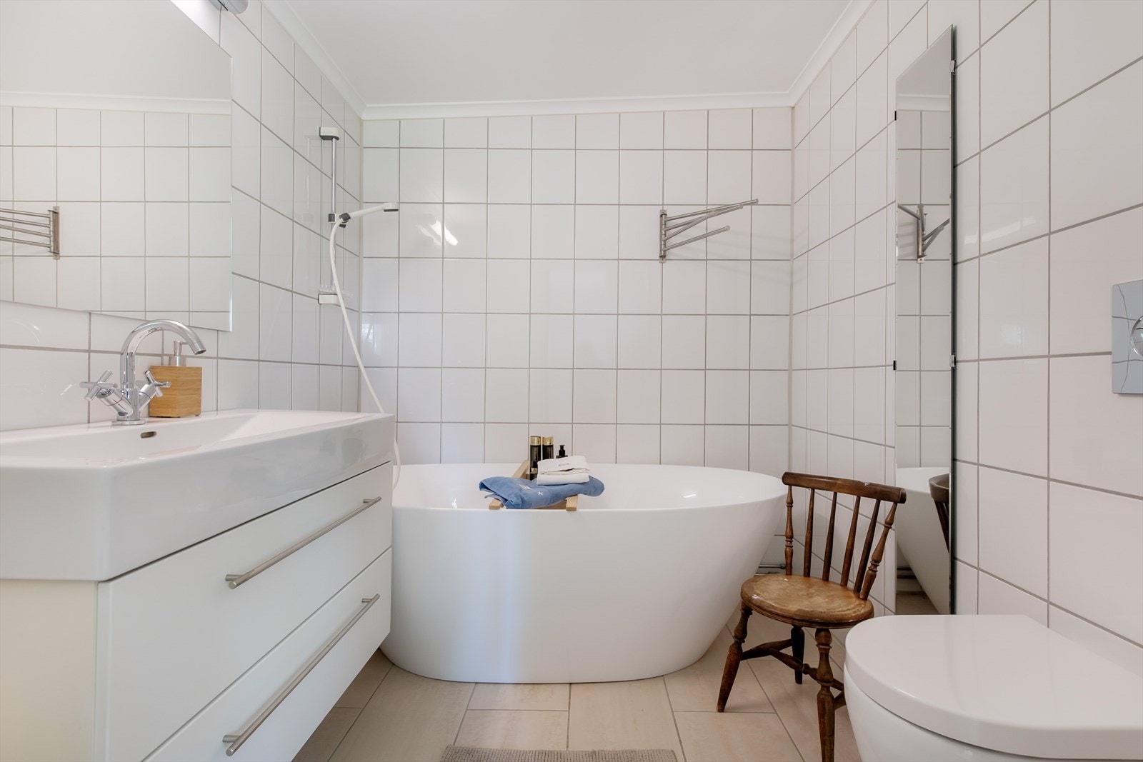 Fra soverommet er det direkte adkomst til eget bad. Badet er romslig, og holdt i nøytrale farge- og materialvalg. Det veggmontert toalett, badekar og baderomsinnredning med skuffer, servant i innredning og speil. Galleribilde