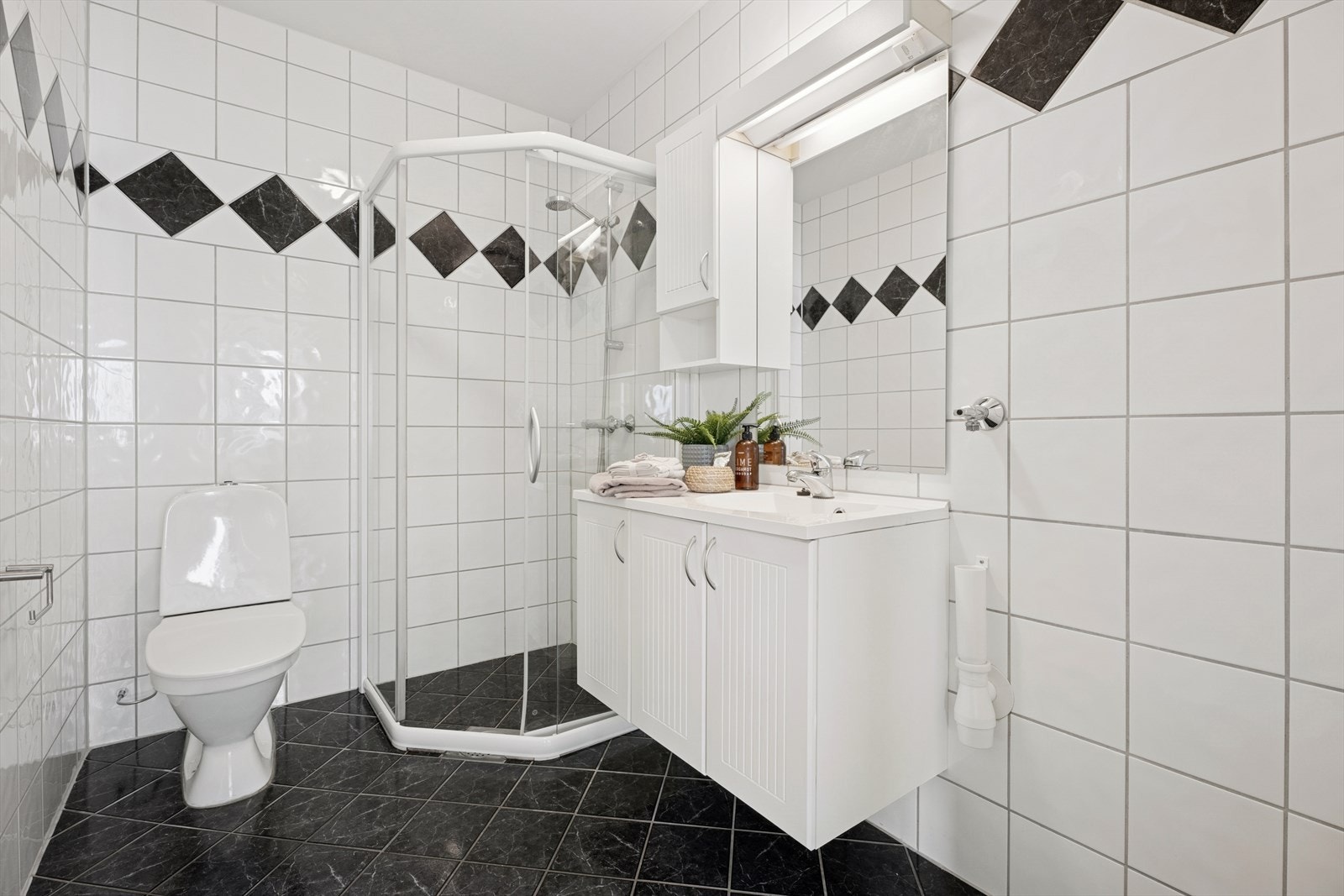 Badet er innredet med servant med underskap, speil med belysning, et gulvmontert toalett og en plassbesparende dusjnisje. Galleribilde