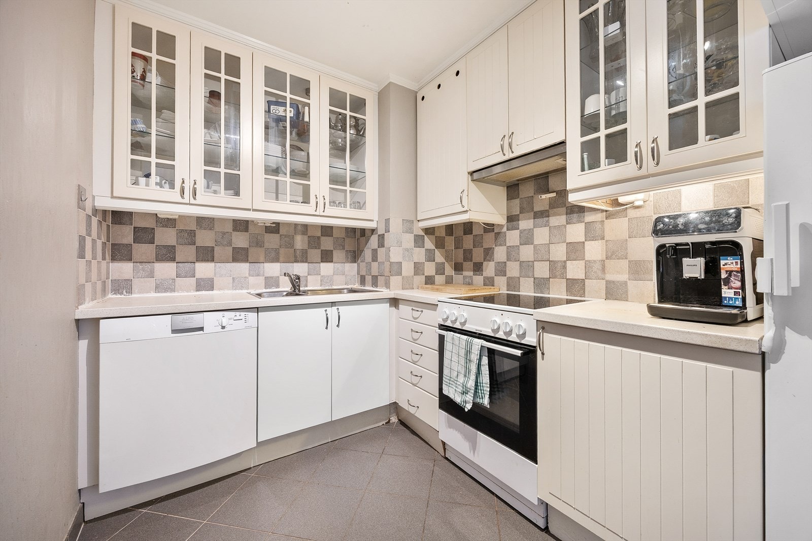 Kjøkkeninnredning med slette fronter, laminat benkeplate og fliser over benk. Galleribilde