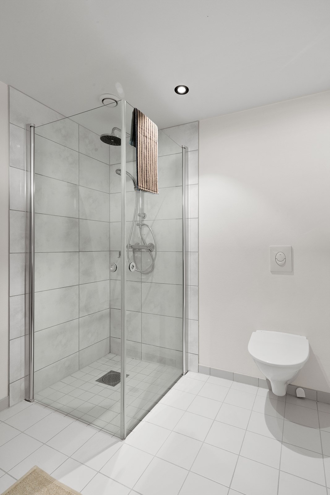 Badet er flislagt i gulv og i dusjsone. Vegghengt toalett glassvegger i dusjhjørnet. Galleribilde