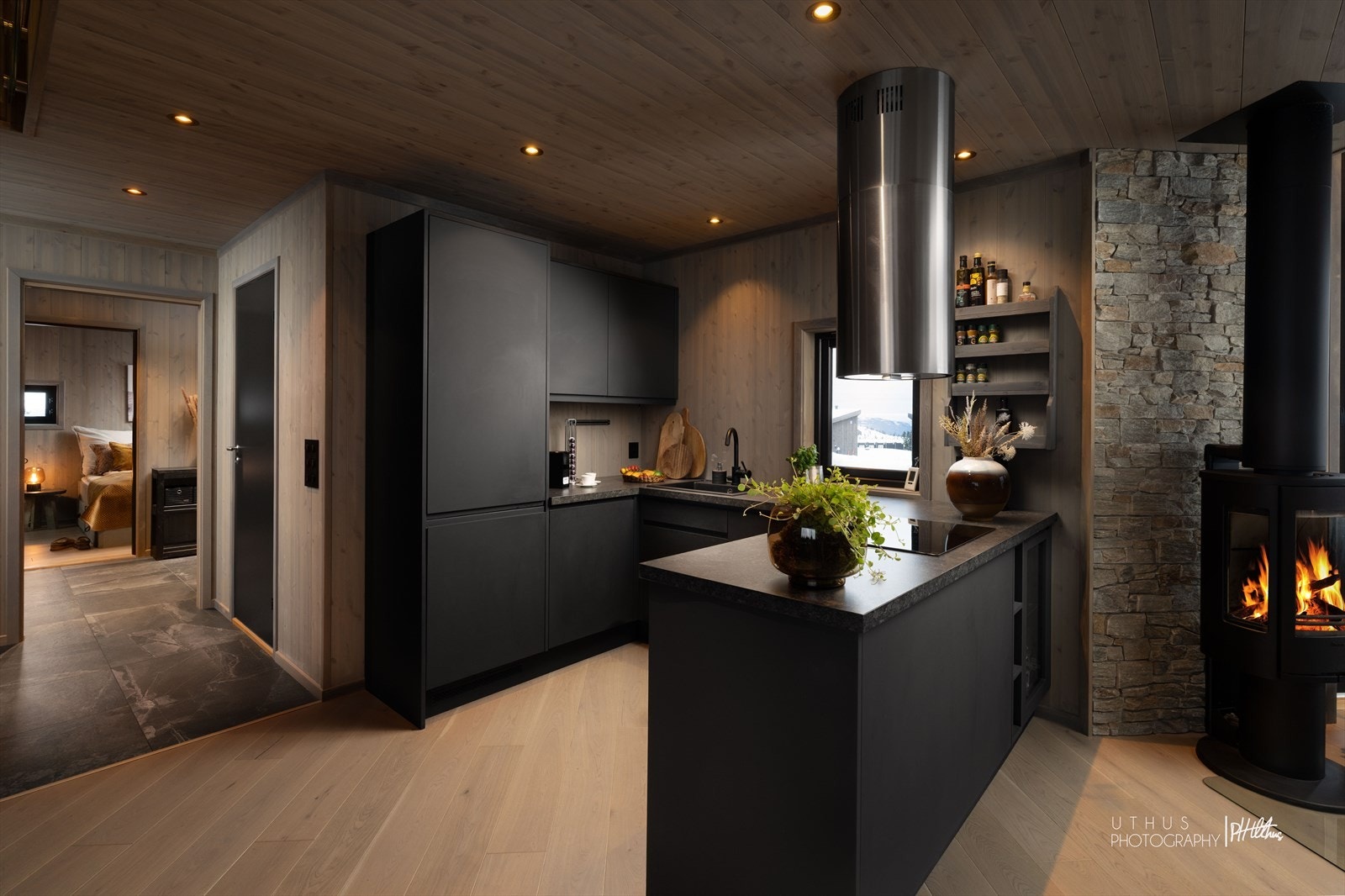 Kjøkkenet er stilrent med mørke, slette fronter og en praktisk kjøkkenøy. Peisovnen gir ekstra varme. Galleribilde