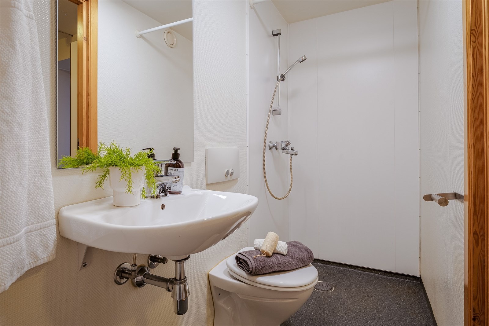 Bad med enkel innredning : servant, dusj, toalett, varmtvannstank og opplegg for vaskemaskin Galleribilde