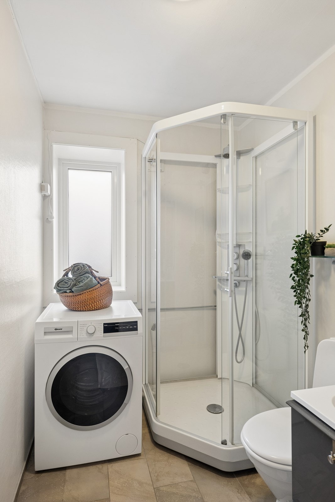 Badet er innredet med toalett, dusjkabinett, heldekkende servant i moderne baderomsinnredning og opplegg til vaskemaskin Galleribilde