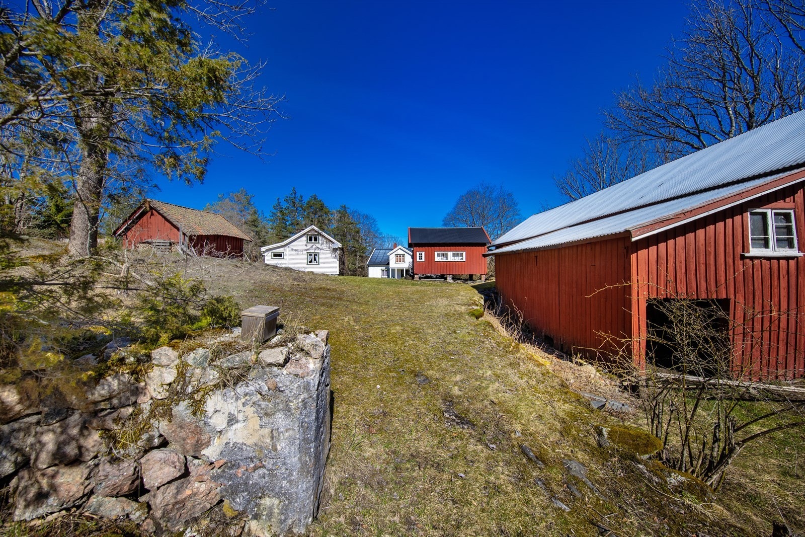 Bildene i annonsen er fra 2022. Dagens eiere har startet med å etablere vei bort til hovedhuset, og uteområdet på bildene samsvarer ikke med hvordan det ser ut i dag. Galleribilde