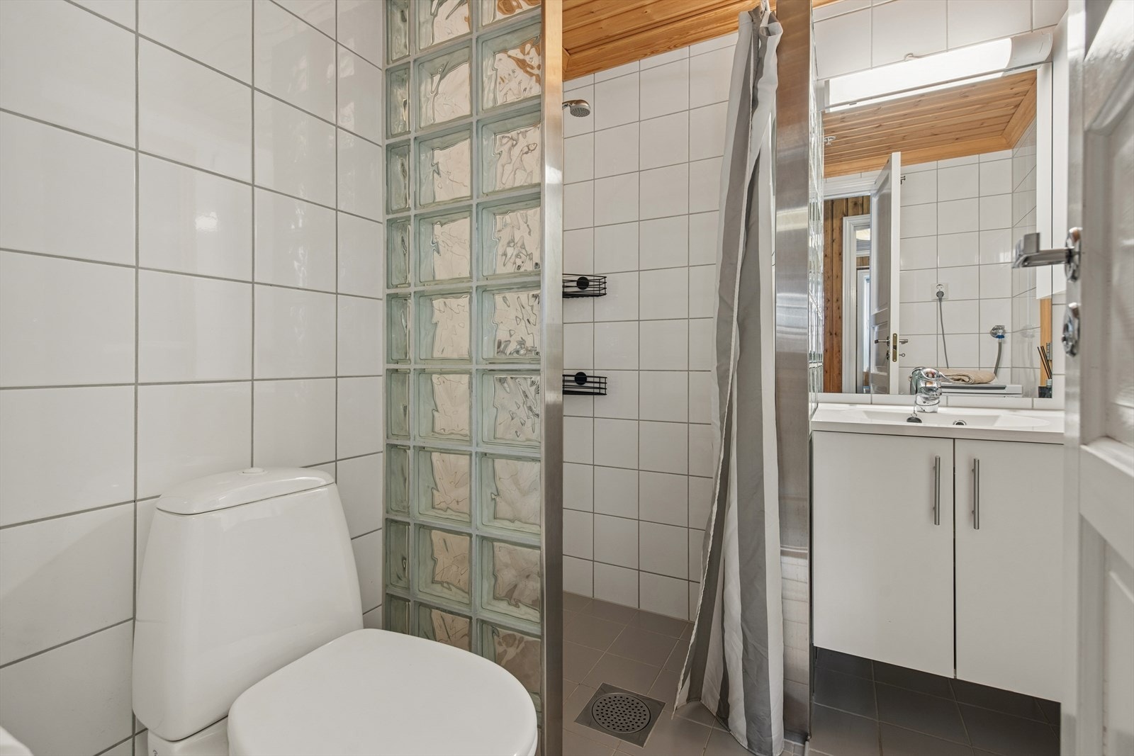 Badet har flislagte overflater med varmekabler, servant med oppbevaring, frittstående toalett, dusjhjørne og elektrisk styrt vifte for ventilasjon. Galleribilde