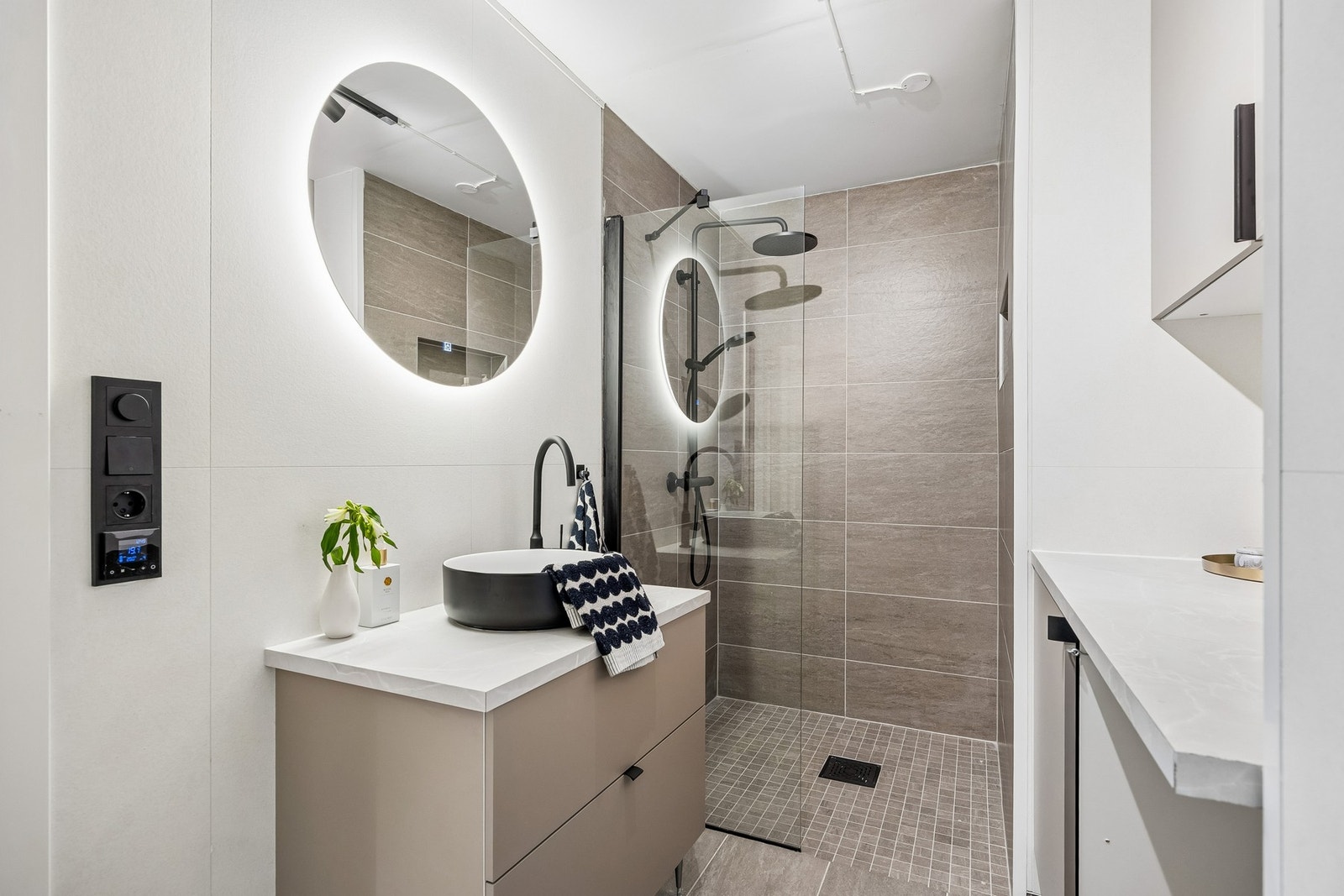 Badet er utstyrt med vegghengt toalett, servantinnredning og dusjhjørne med glassdører, samt egen sone med opplegg for vaskemaskin. Galleribilde