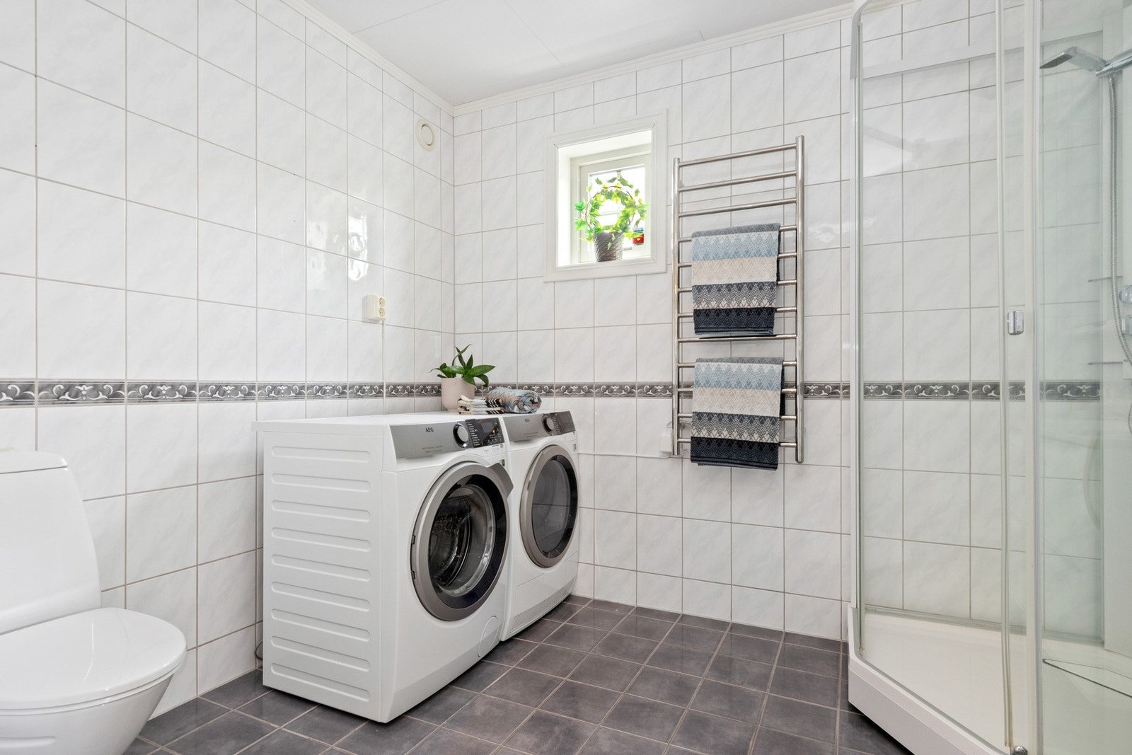 Badet er romslig og innredet med hvite veggfliser og mørke gulvfliser. Galleribilde