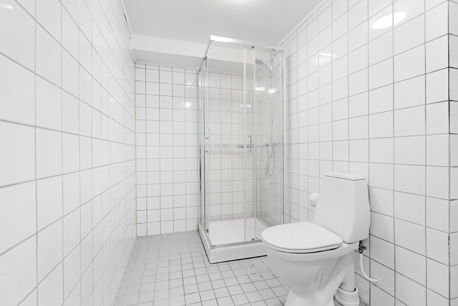 Badet er utstyrt med et gulvmontert toalett, en servantinnredning, et dusjkabinett samt opplegg for vaskemaskin Galleribilde