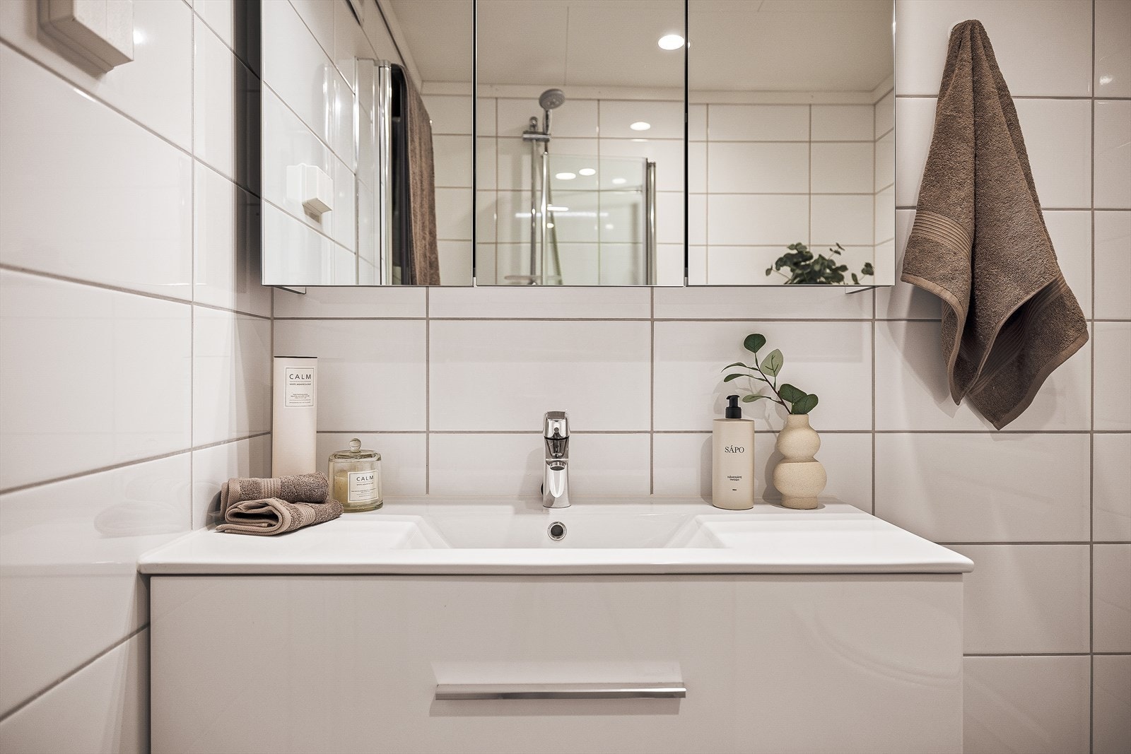 Baderomsinnredningen har et tidløs design med glatte, hvite fronter og integrert belysning i speilet. Galleribilde