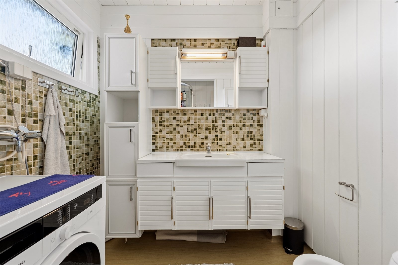 Badet er utstyrt med baderomsinnredning med nedfelt servant, toalett, dusjkabinett og opplegg for vaskemaskin Galleribilde